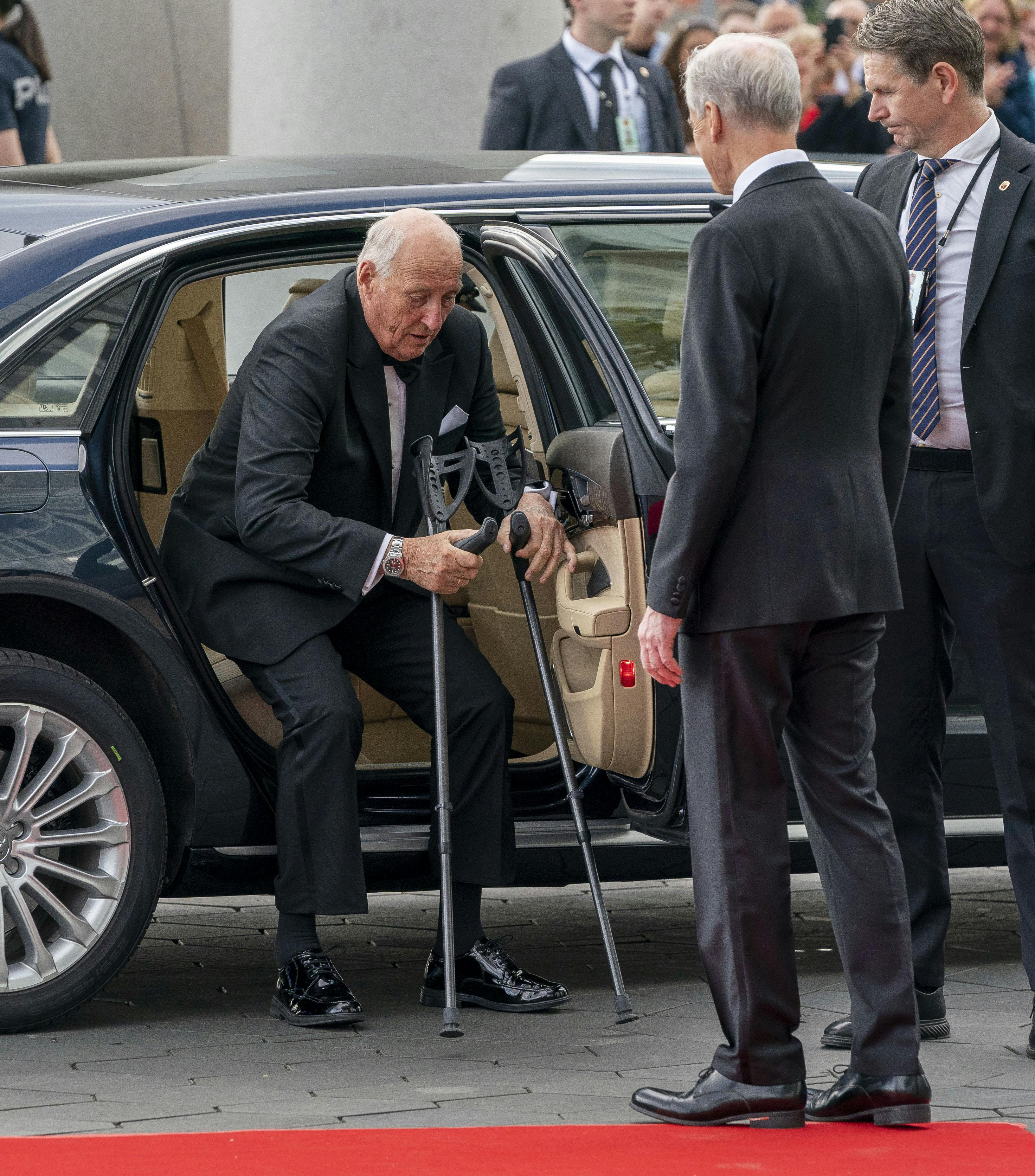 Kong Harald træder ud af bilen med sine krykker.