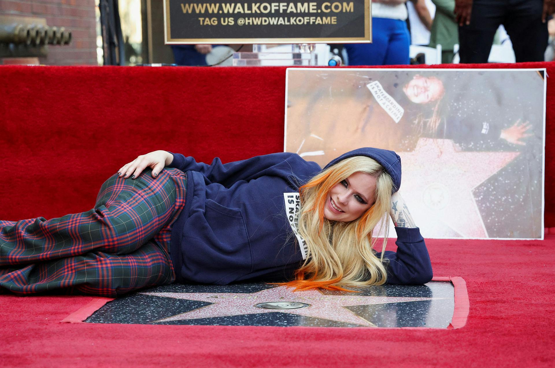 Avril Lavigne med sin stjerne på Walk of Fame. I baggrunden er et billede af en 16-årig Avril Lavigne, første gang hun var på Hollywood Boulevard, dengang var det Tom Cruises stjerne, hun lå ved.