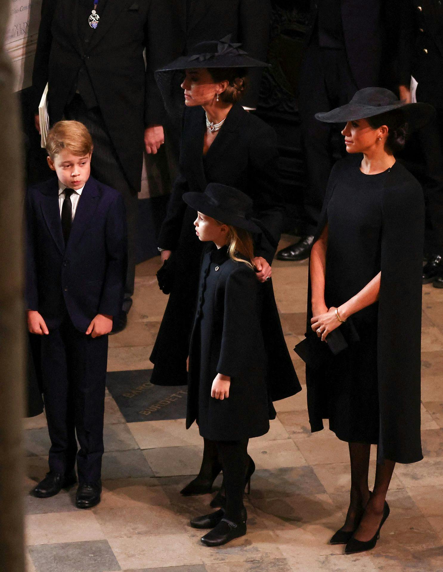 Prinsesse Charlotte med prins George, Kate Middleton og Meghan Markle (th.).
