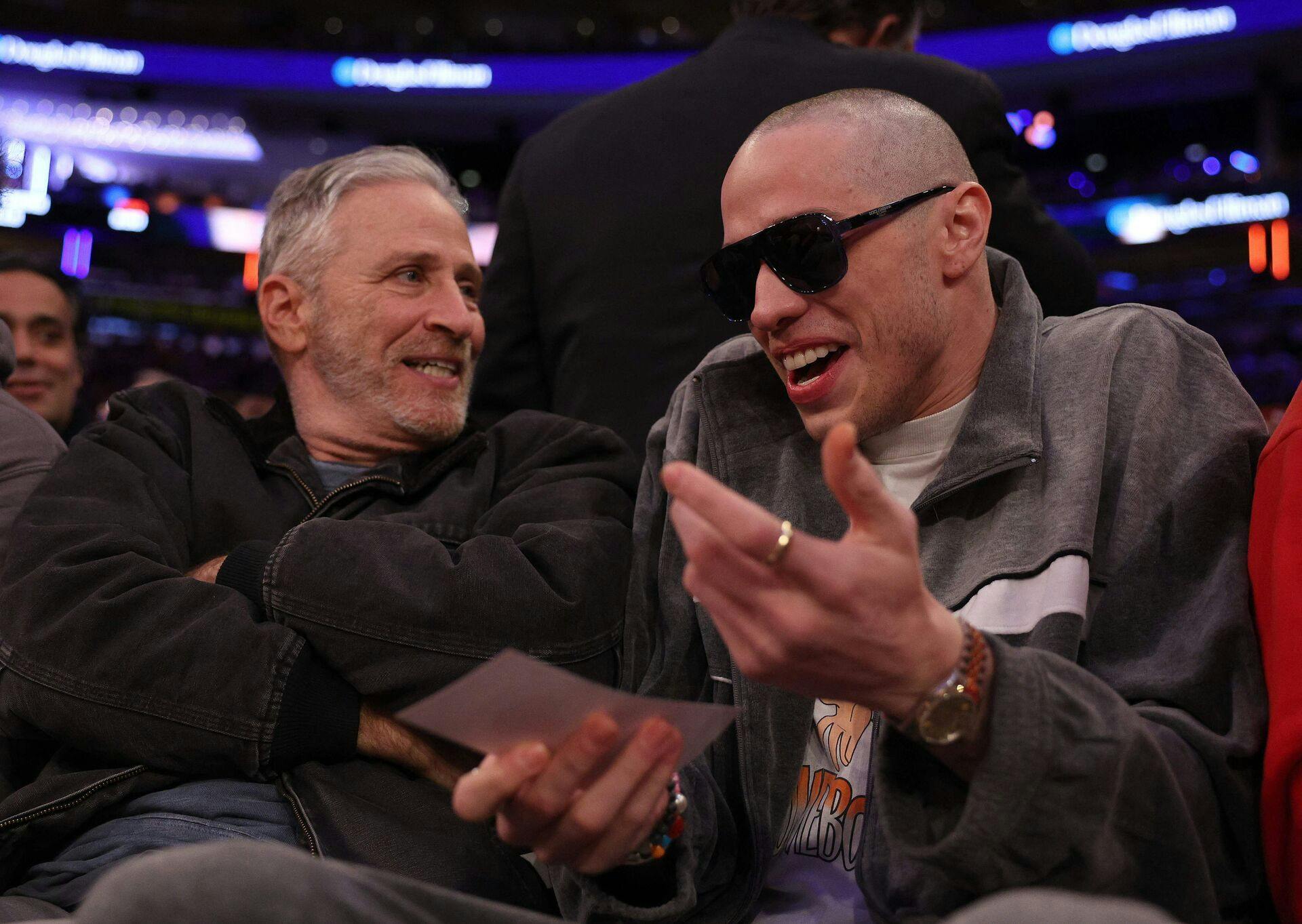 Pete Davidson ved siden af Jon Stewart til basketballkampen.
