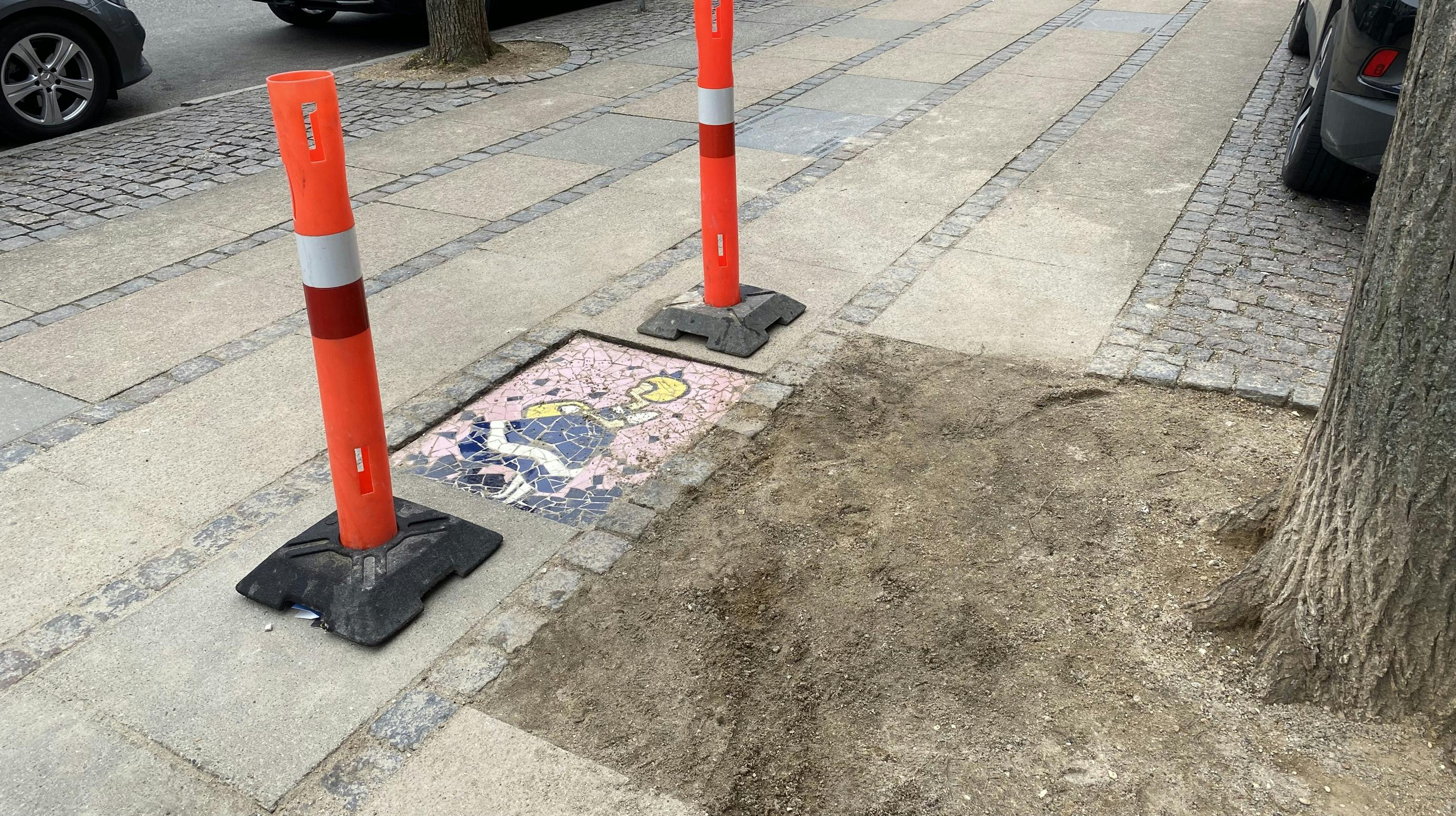 Mandag morgen har by-, kultur-, og miljøforvaltningen sat afspærringscylindre op ved mosaikflisen - nu skal lokalpolitikerne afgøre, om den skal blive liggende. 