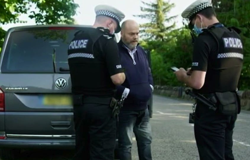 En brødbetynget Anders Holch Povlsen modtager sin fartbøde af de to skotske betjente. 