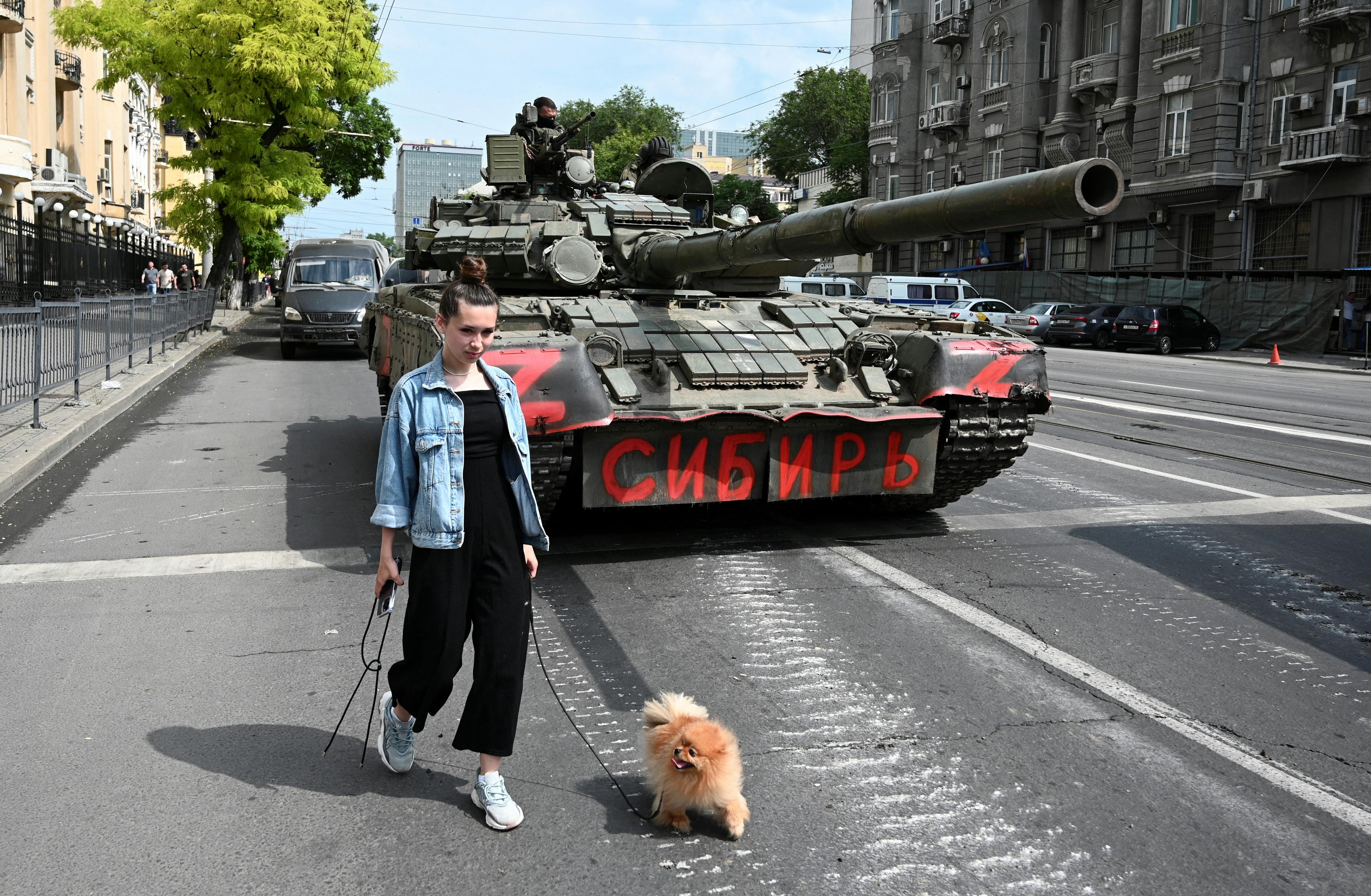 A woman with a dog walks past a tank as fighters of Wagner private mercenary group are deployed in a street near the headquarters of the Southern Military District in the city of Rostov-on-Don, Russia, June 24, 2023. A sign on a tank reads: "Siberia". REUTERS/Stringer