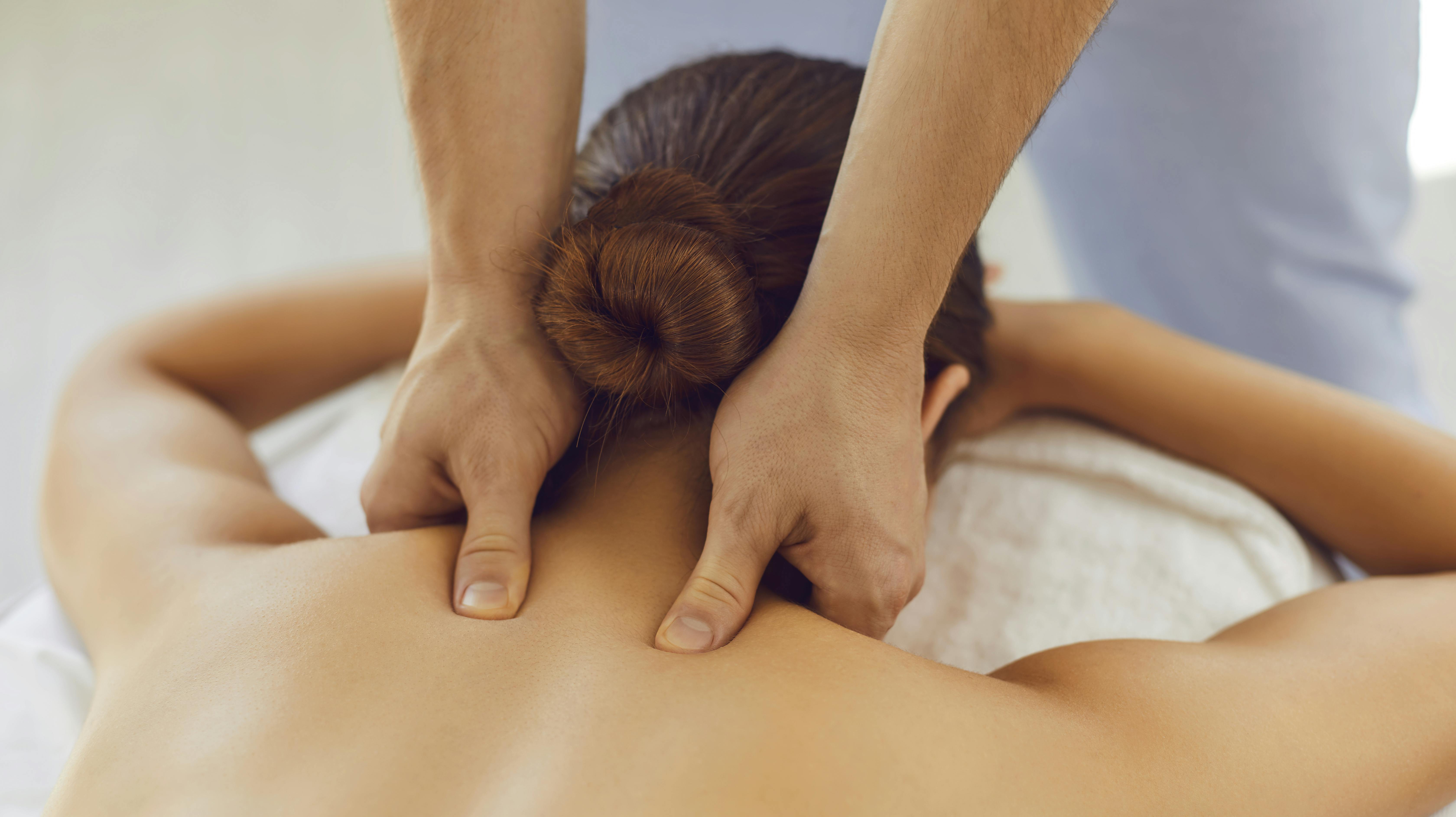 Men's hands do a therapeutic neck massage for a girl lying on a massage couch in a bright massage spa. Acupressure massage in spa centre. Body therapy for healthy lifestyle. Close up.