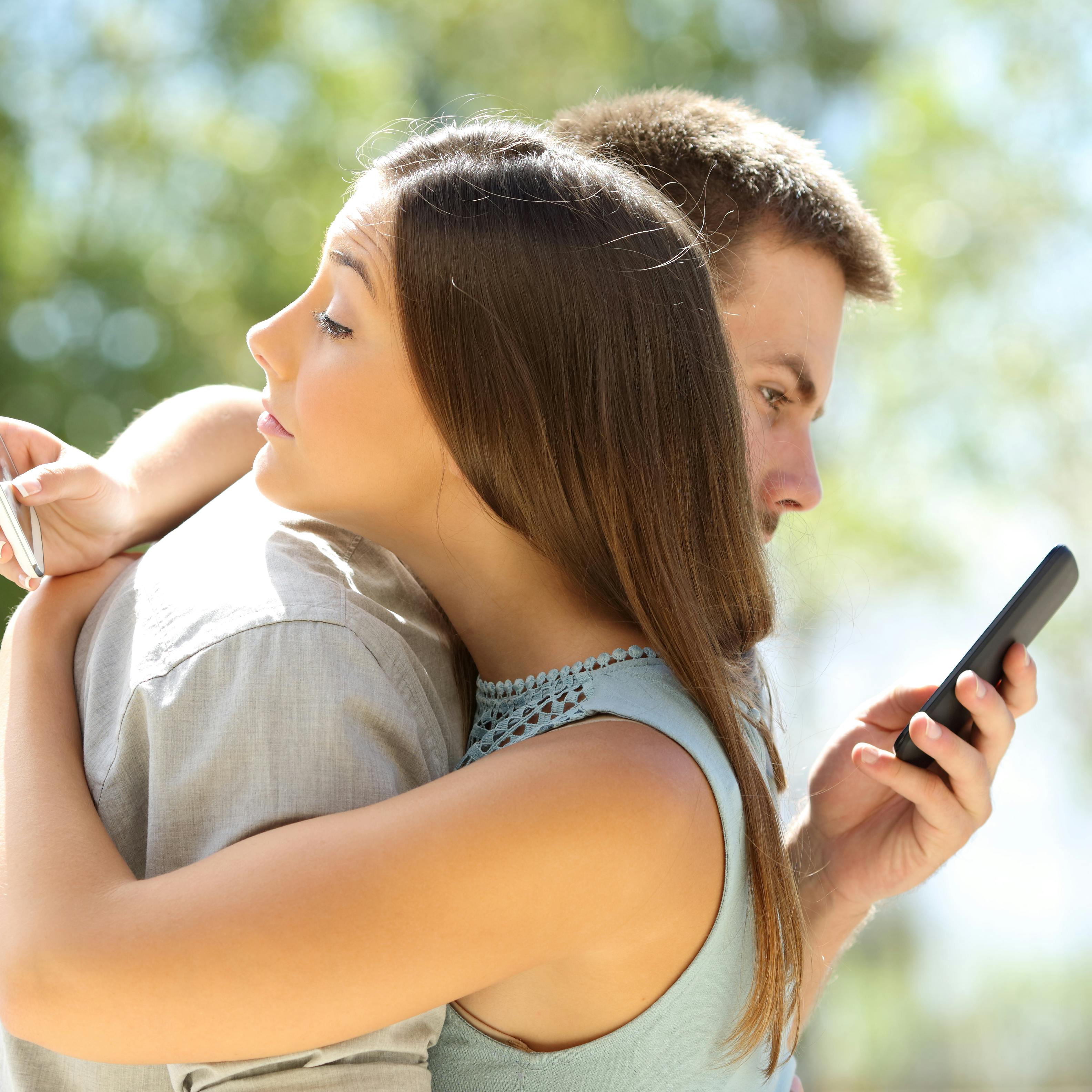 Couple of cheaters hugging and texting everyone on their smart phones