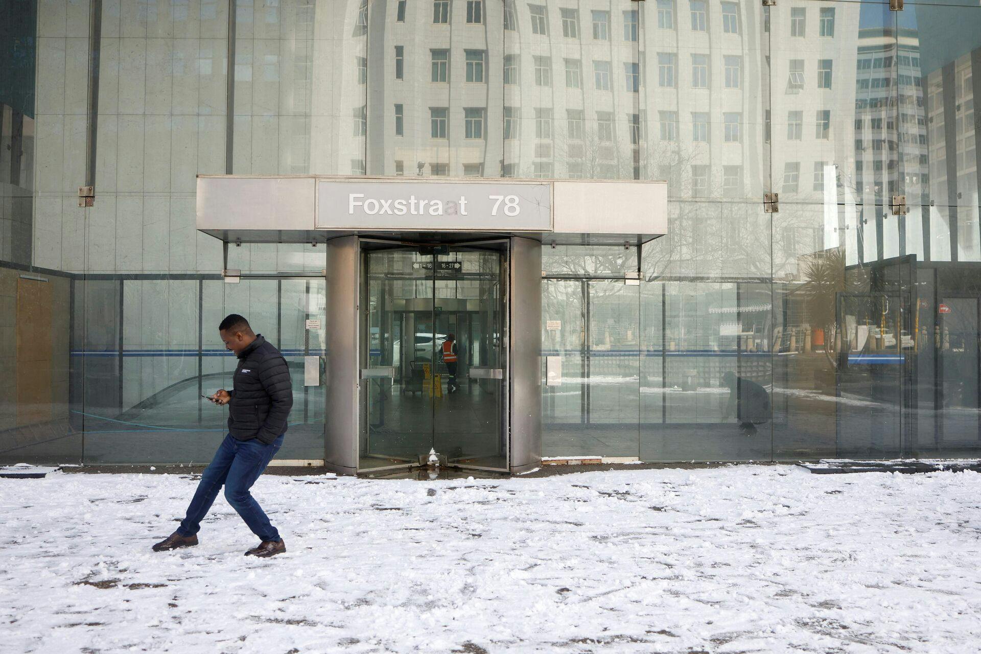 A man stands on a snowy plaza in front of an office building in Johannesburg on July 10, 2023. (Photo by Wikus de Wet / AFP)