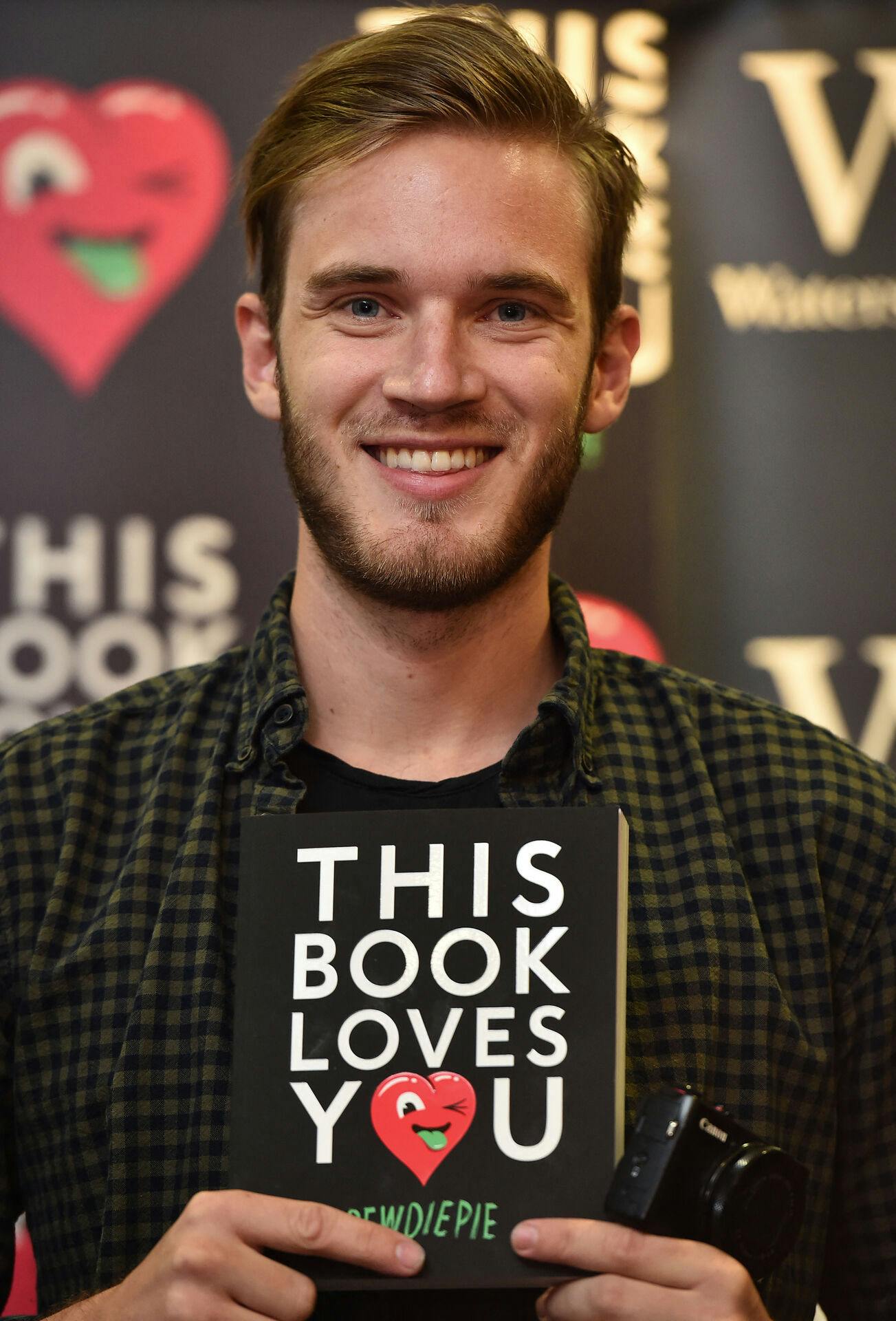 Swedish video game commentator Felix Kjellberg, aka PewDiePie poses with his new book, 'This book loves you' at an event in central London, on October 18, 2015. AFP PHOTO / BEN STANSALL. BEN STANSALL / AFP