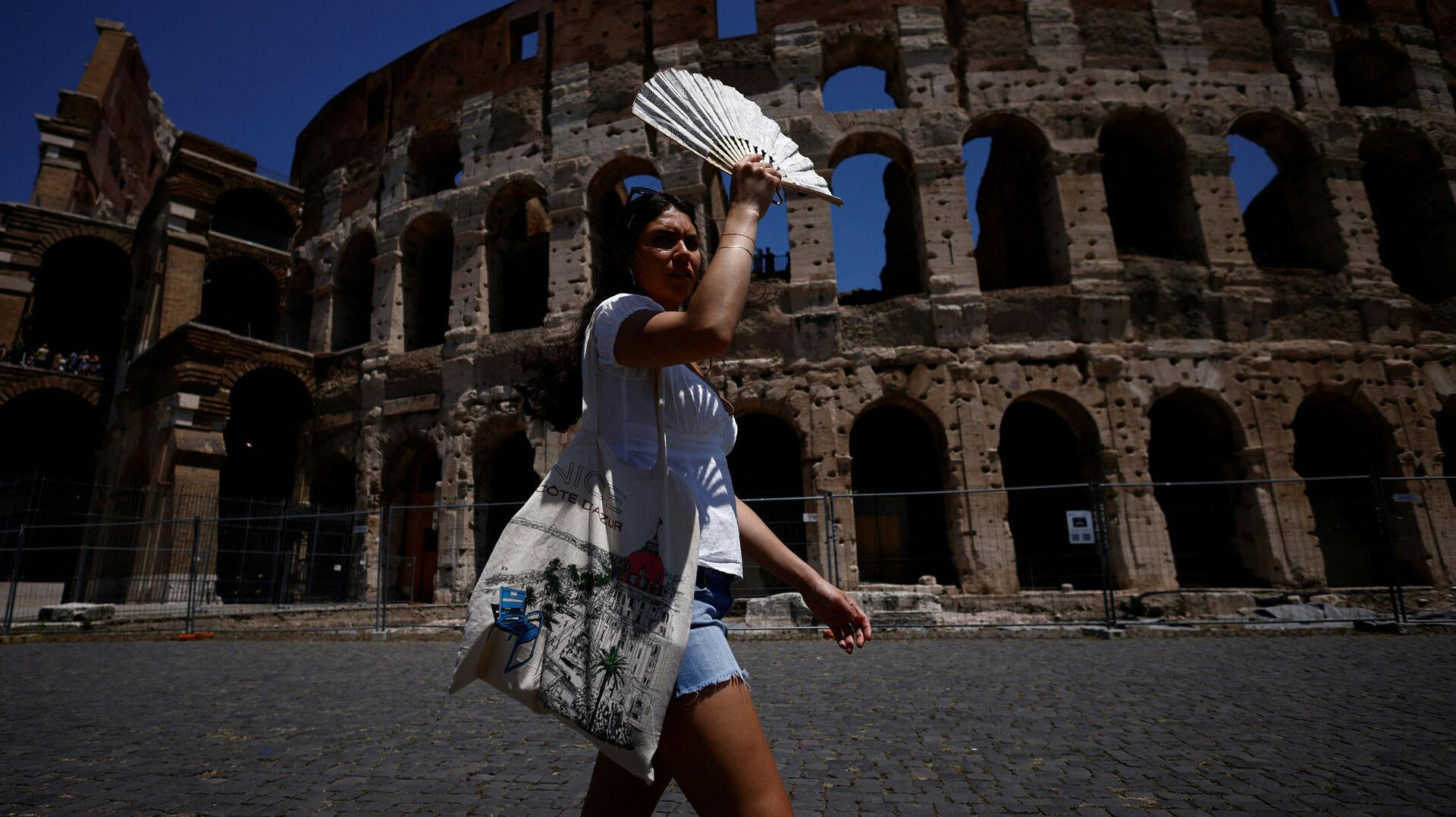 Michelle from the U.S. uses a fan to shelter from the sun near the Colosseum during a heatwave across Italy, in Rome, Italy July 11, 2023. REUTERS/Guglielmo Mangiapne