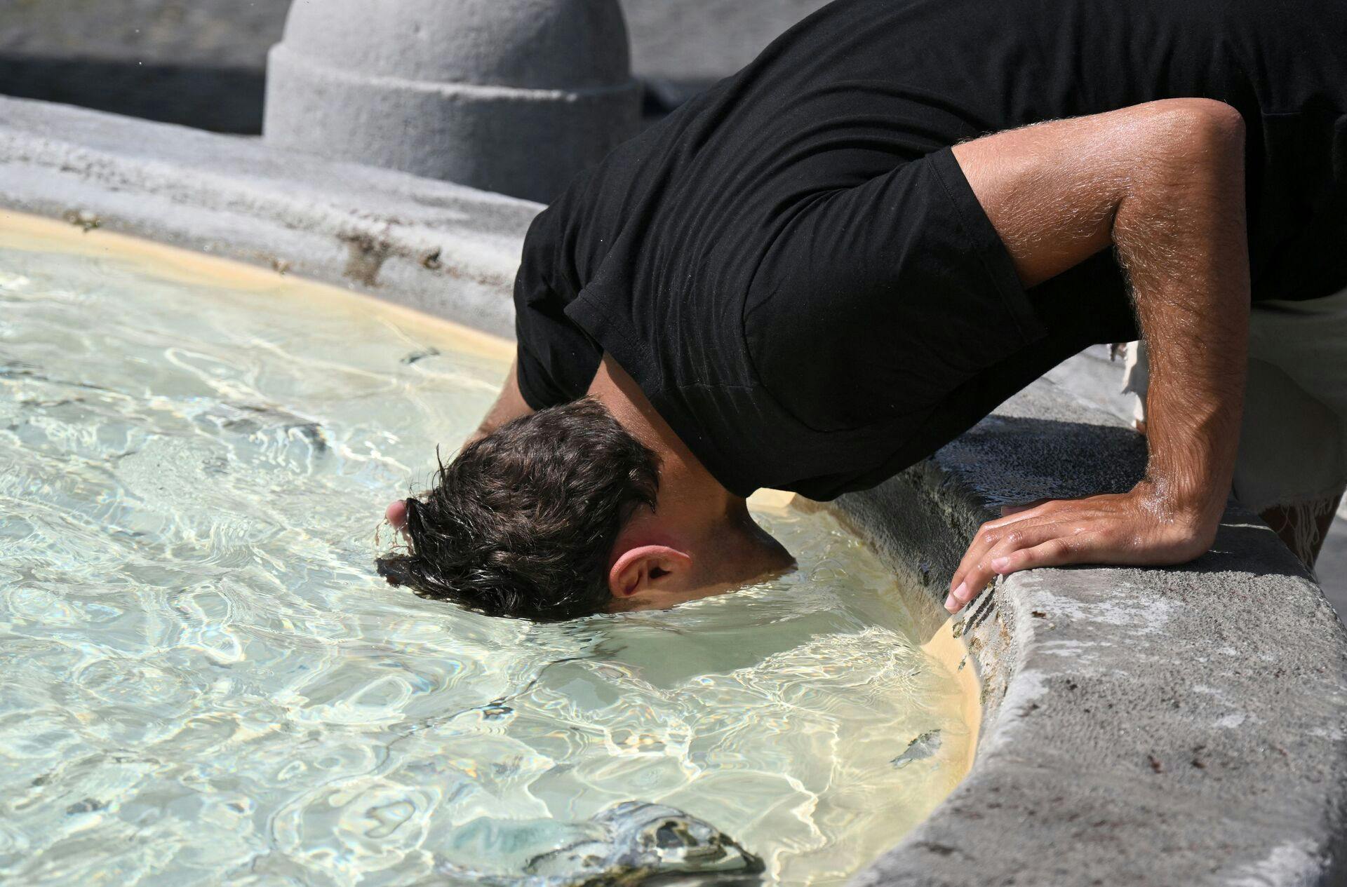 A man puts his head in the water to cool off at the fountain in Piazza del Popolo in Rome, on July 18, 2023. Europe braced for new high temperatures on July 18, 2023, under a relentless heatwave and wildfires that have scorched swathes of the Northern Hemisphere, forcing the evacuation of 1, 200 children close to a Greek seaside resort. (Photo by Tiziana FABI / AFP)