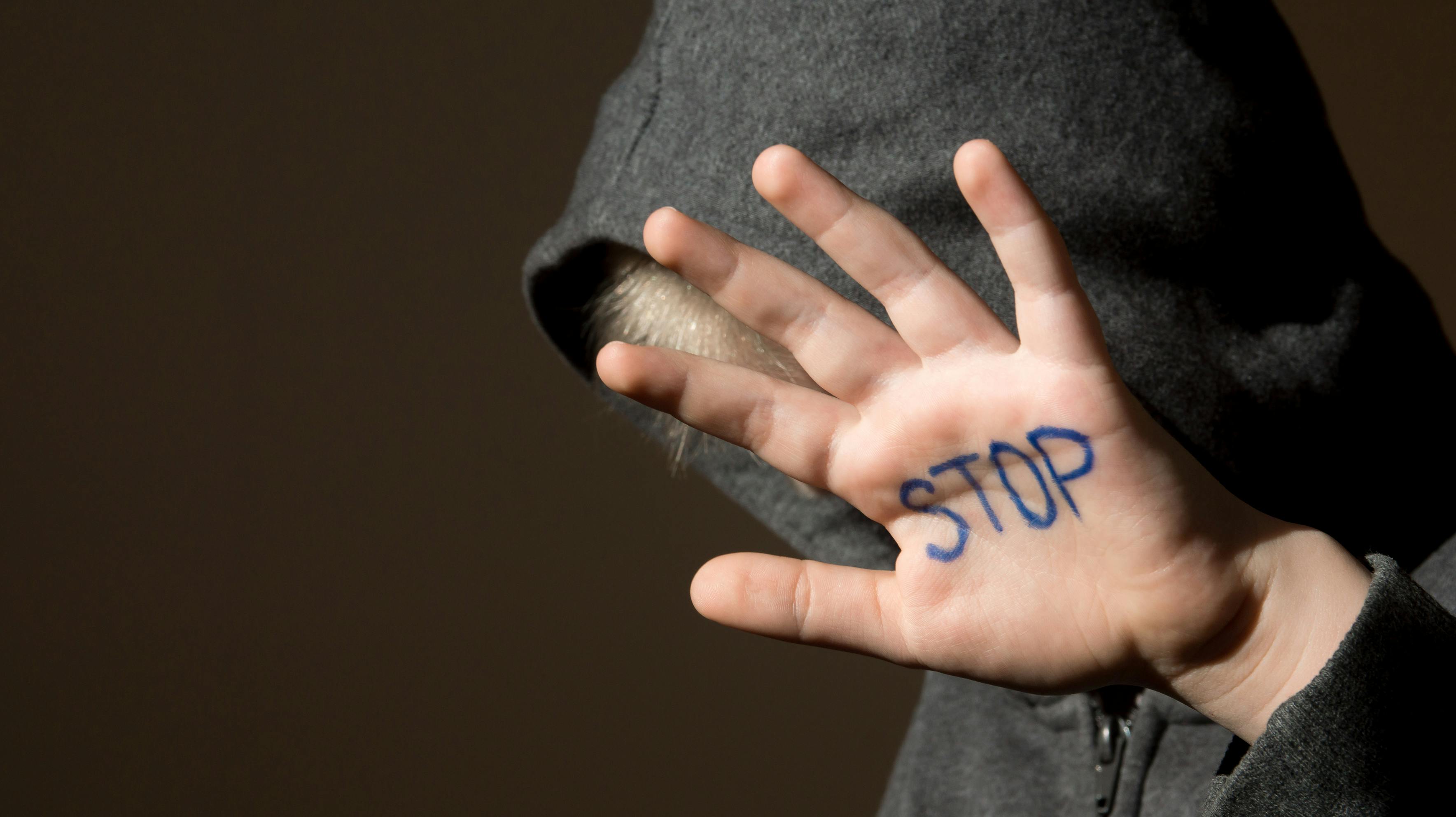 Upset abused frightened little child (boy), stop hand jesture close up horizontal dark portrait with copy space