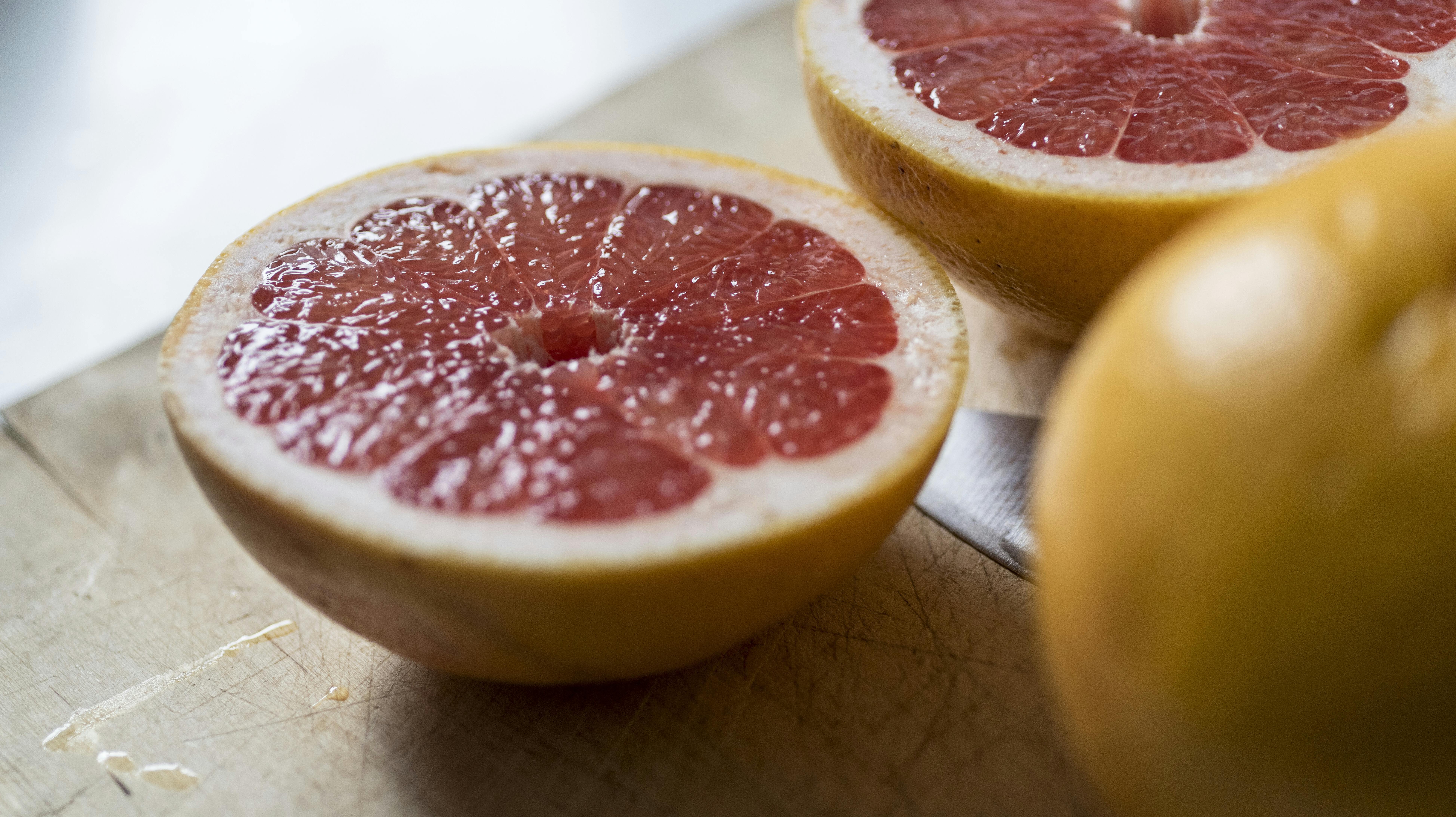 Rød grape eller grapefrugt, som er gennemskåret på spækbræt af skarp kniv. På køkkenbord i lejlighed
