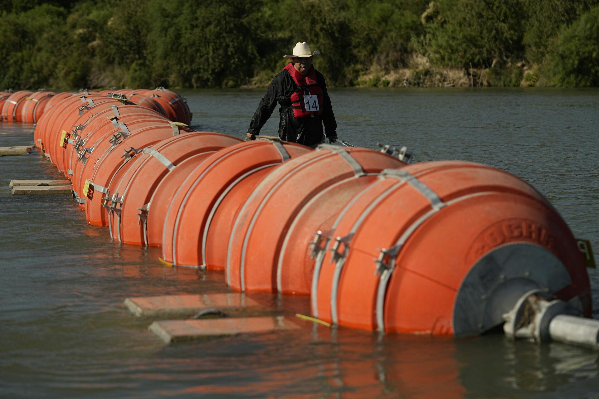 A kayaker walks past large buoys being used as a floating border barrier on the Rio Grande Tuesday, Aug. 1, 2023, in Eagle Pass, Texas. (AP Photo/Eric Gay)