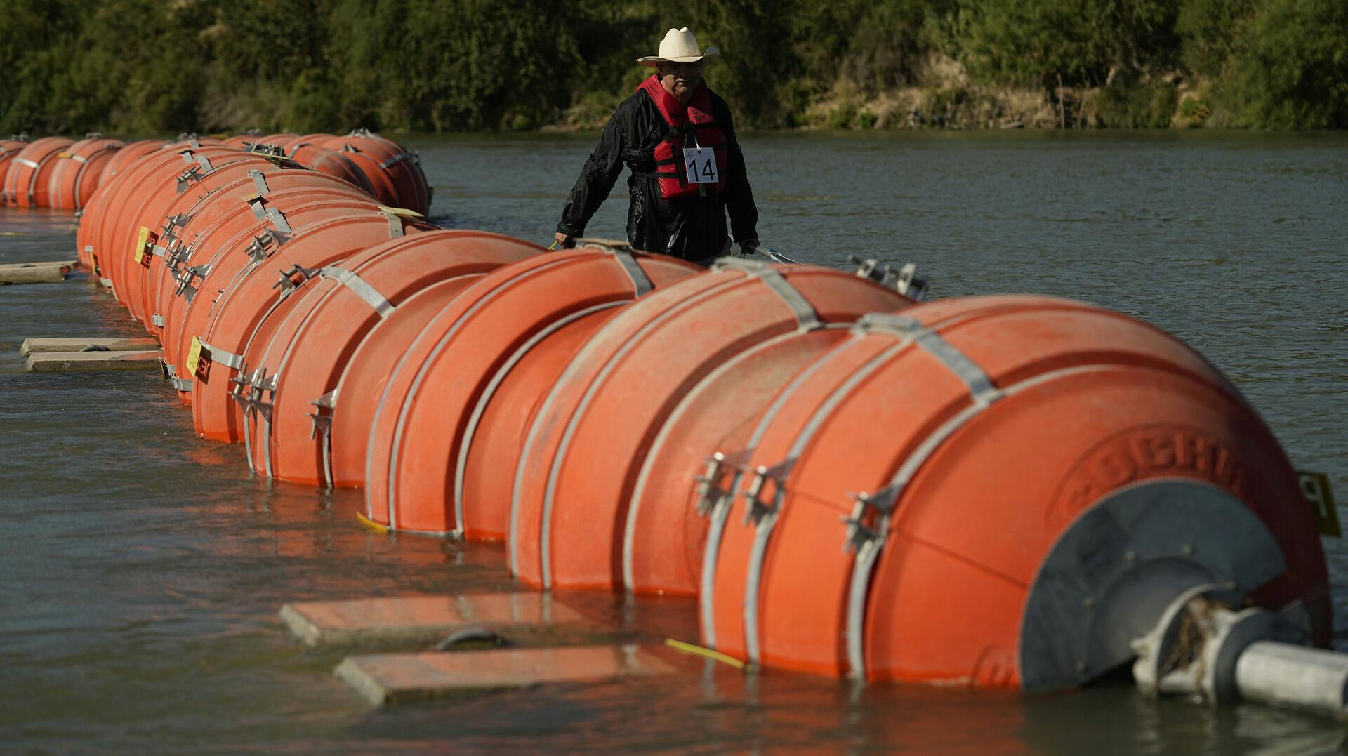 A kayaker walks past large buoys being used as a floating border barrier on the Rio Grande Tuesday, Aug. 1, 2023, in Eagle Pass, Texas. (AP Photo/Eric Gay)