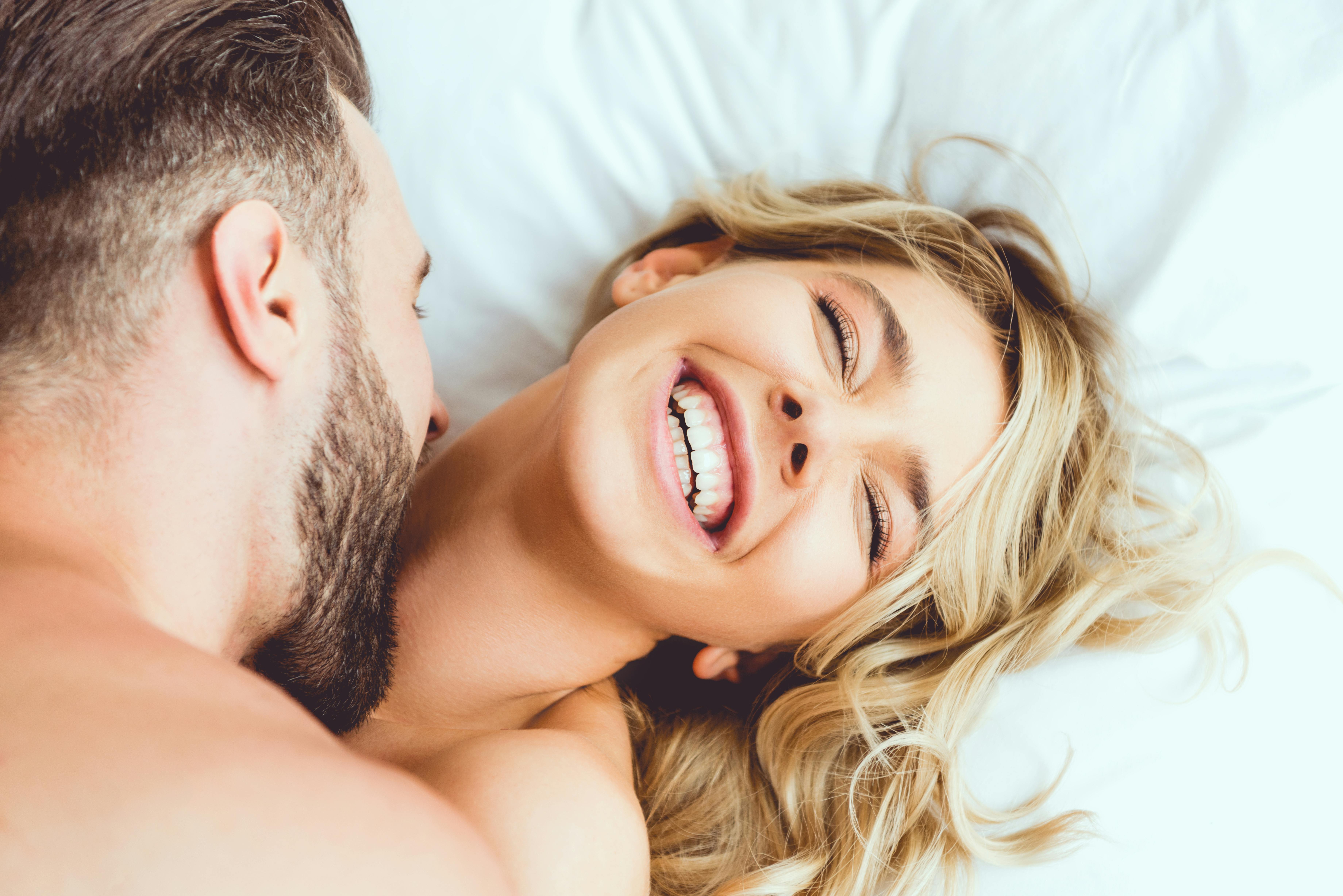 cropped view of young man biting laughing girlfriend while lying in bed