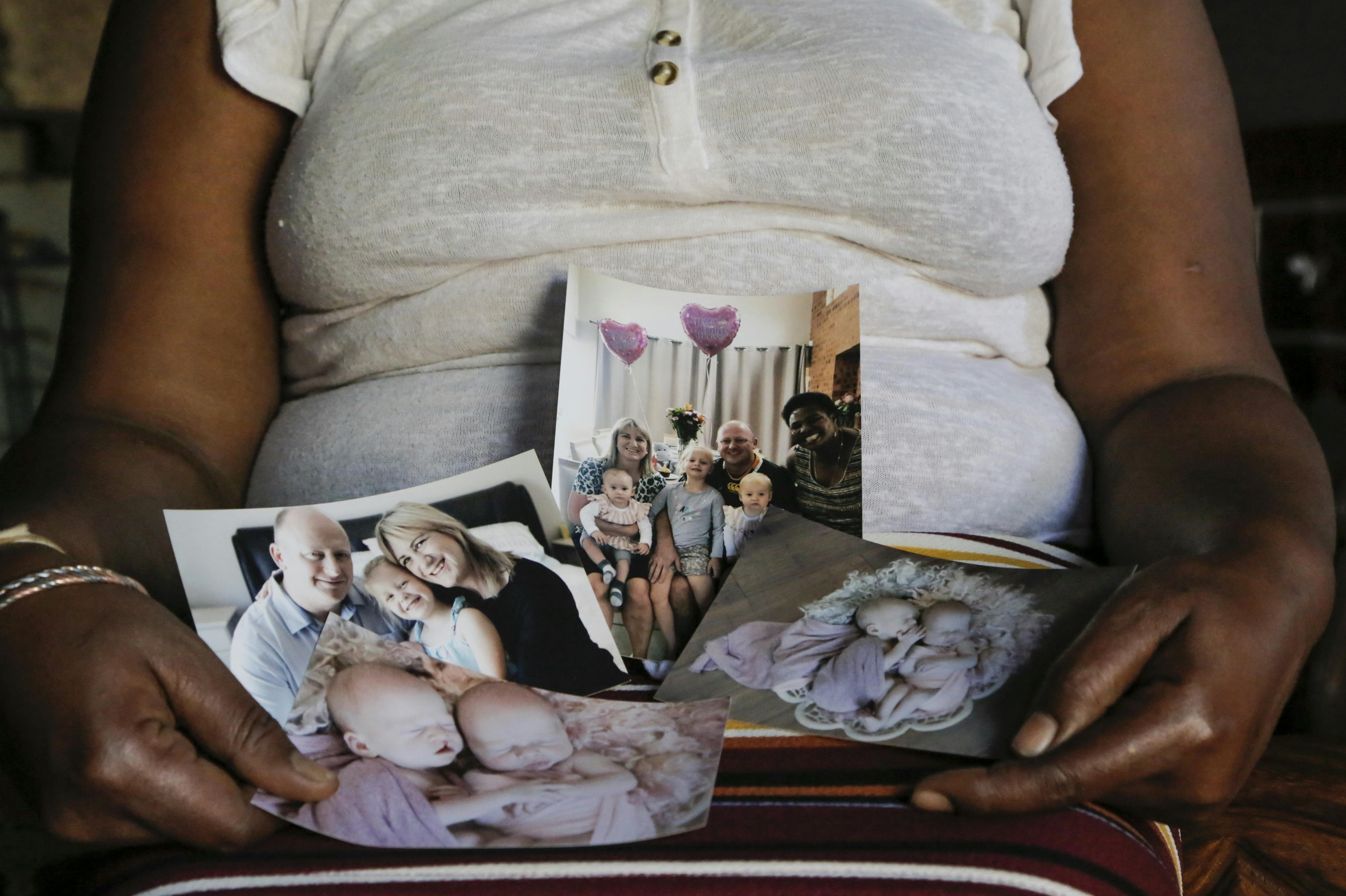 FILE - In this Sept. 17, 2021, file photo, Mandy Sibanyoni, nanny of the three daughters of Graham and Lauren Dickason, holds photographs of the Dickason family in her home in Pretoria, South Africa. People in the town of Timaru are planning an evening vigil outside the home of three young girls, Thursday, Sept. 23, 2021, who were killed last week in a crime that shocked New Zealand. The girls' mother Lauren Dickason has been charged with murder. (AP Photo/Sebabatso Mosamo, File)