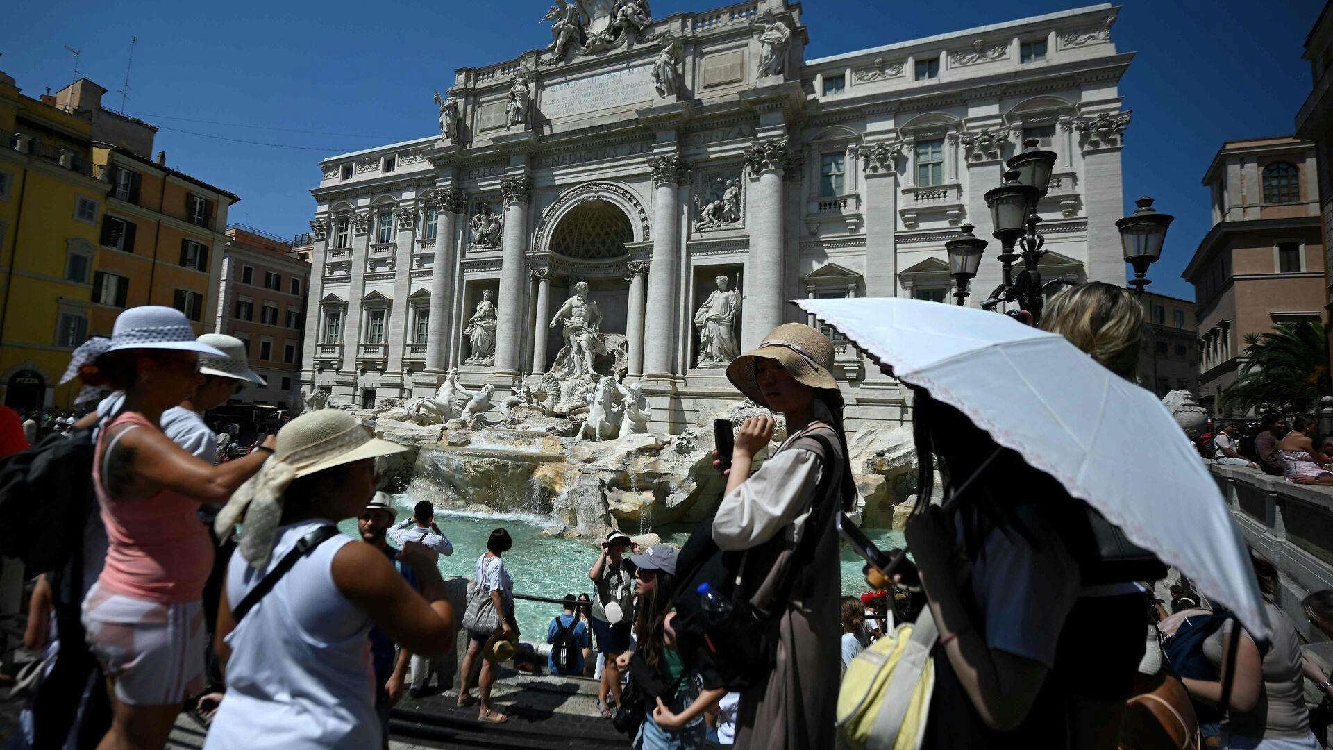 Tourist protect themselves with hats and umbrella at the Trevi Fountain during a heatwave in Rome on August 21 2023. (Photo by Filippo MONTEFORTE / AFP)