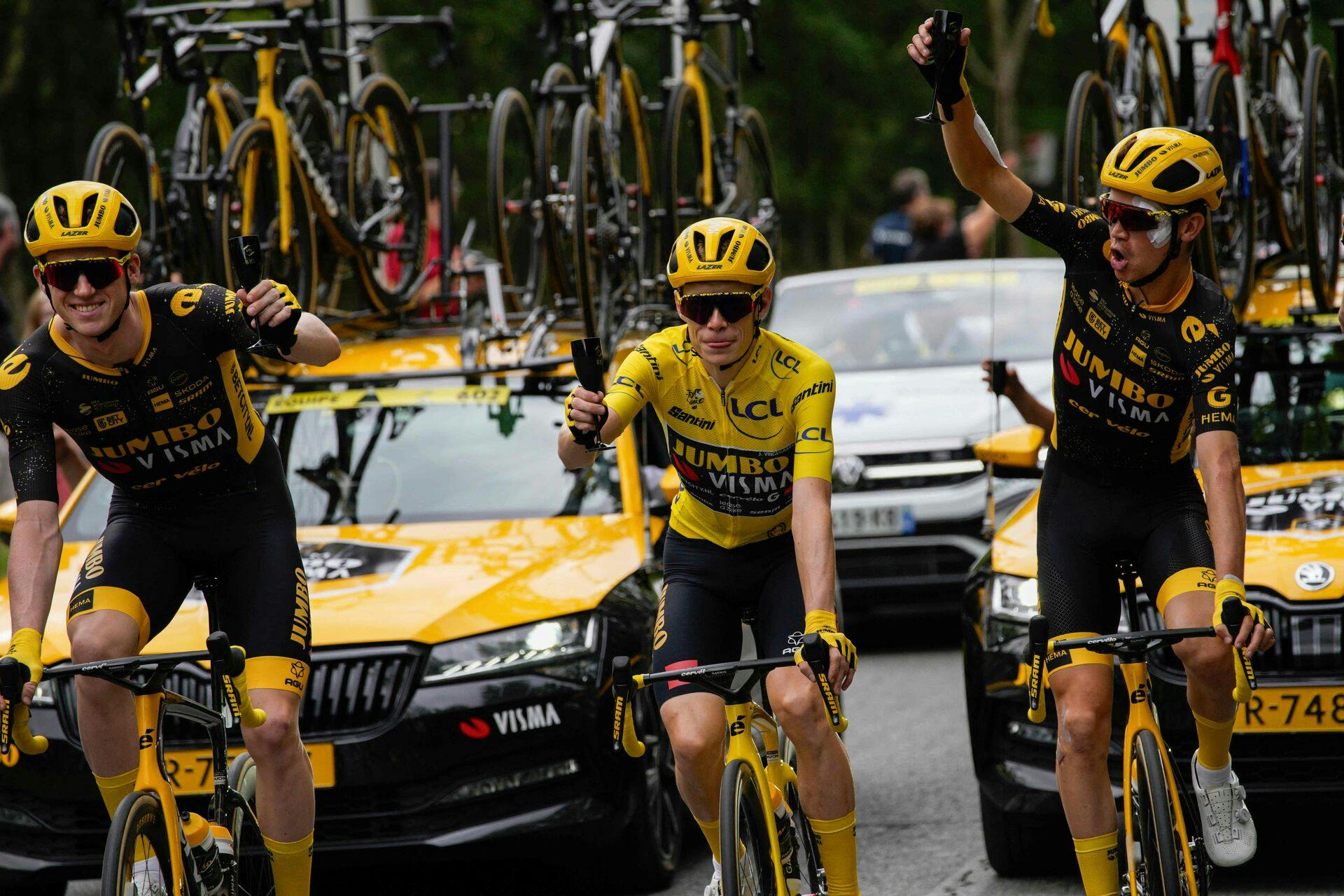 Jumbo-Visma's Danish rider Jonas Vingegaard wearing the overall leader's yellow jersey celebrates with champagne WITH Jumbo-Visma's Belgian rider Nathan Van Hooydonck (L) and Jumbo-Visma's US rider Sepp Kuss (R) as he cycles during the 21st and final stage of the 110th edition of the Tour de France cycling race, 115 km between Saint-Quentin-en-Yvelines and the Champs-Elysees in Paris, on July 23, 2023. (Photo by Daniel Cole / POOL / AFP)