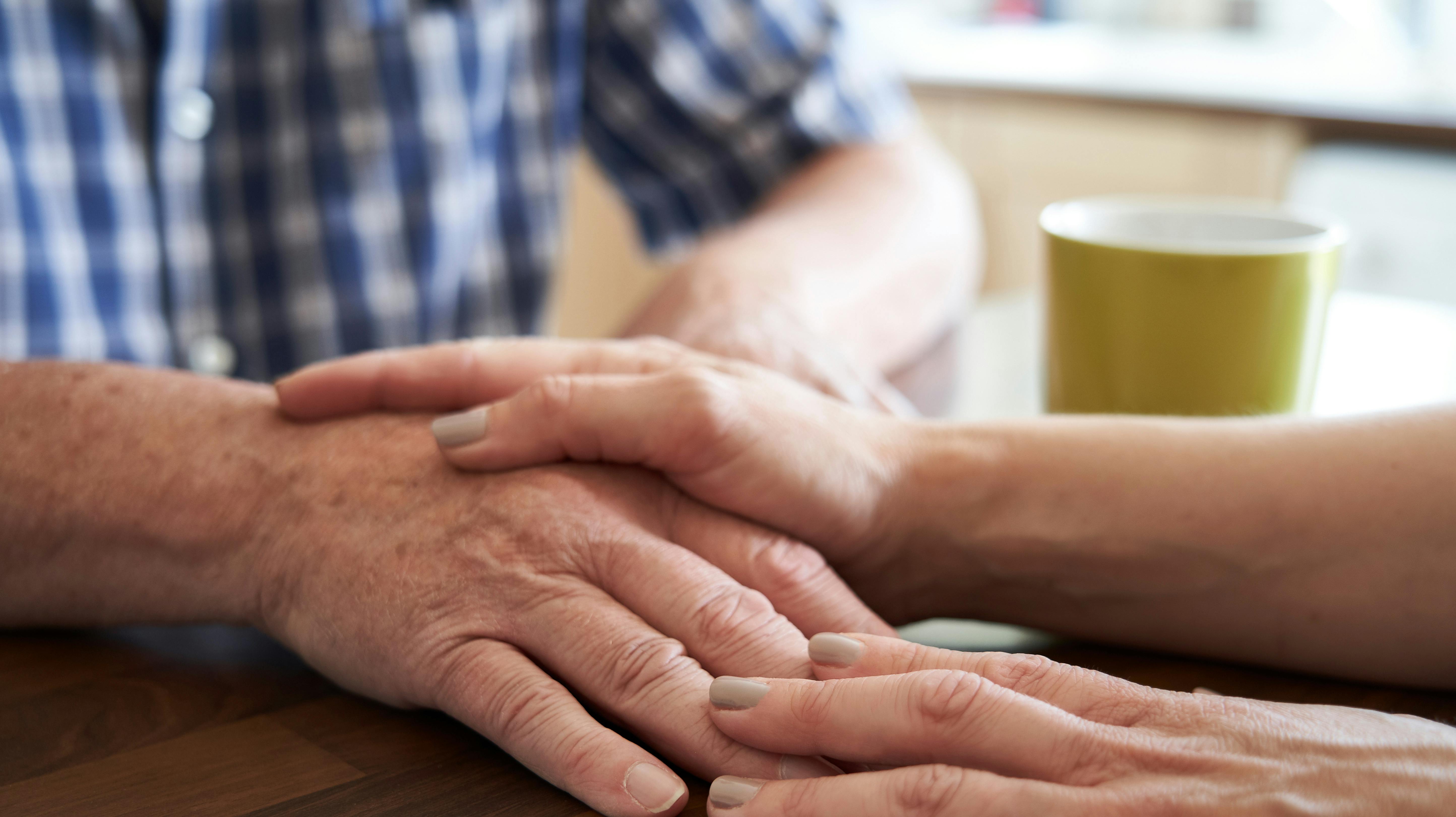 Close Up Of Woman Comforting Unhappy Senior Man Sitting In Kitchen At Home