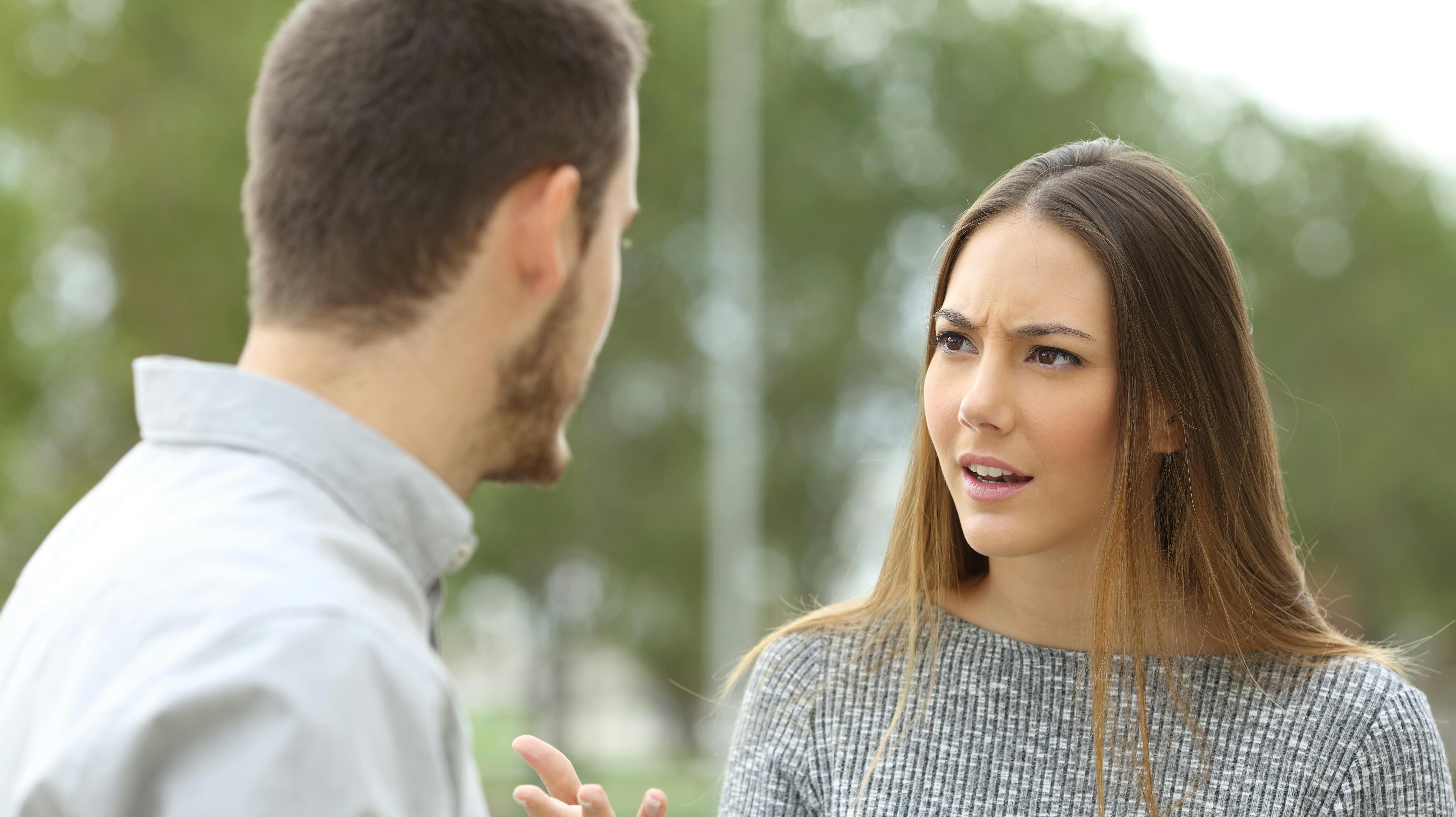 Couple talking seriously outdoors in a park with a green background