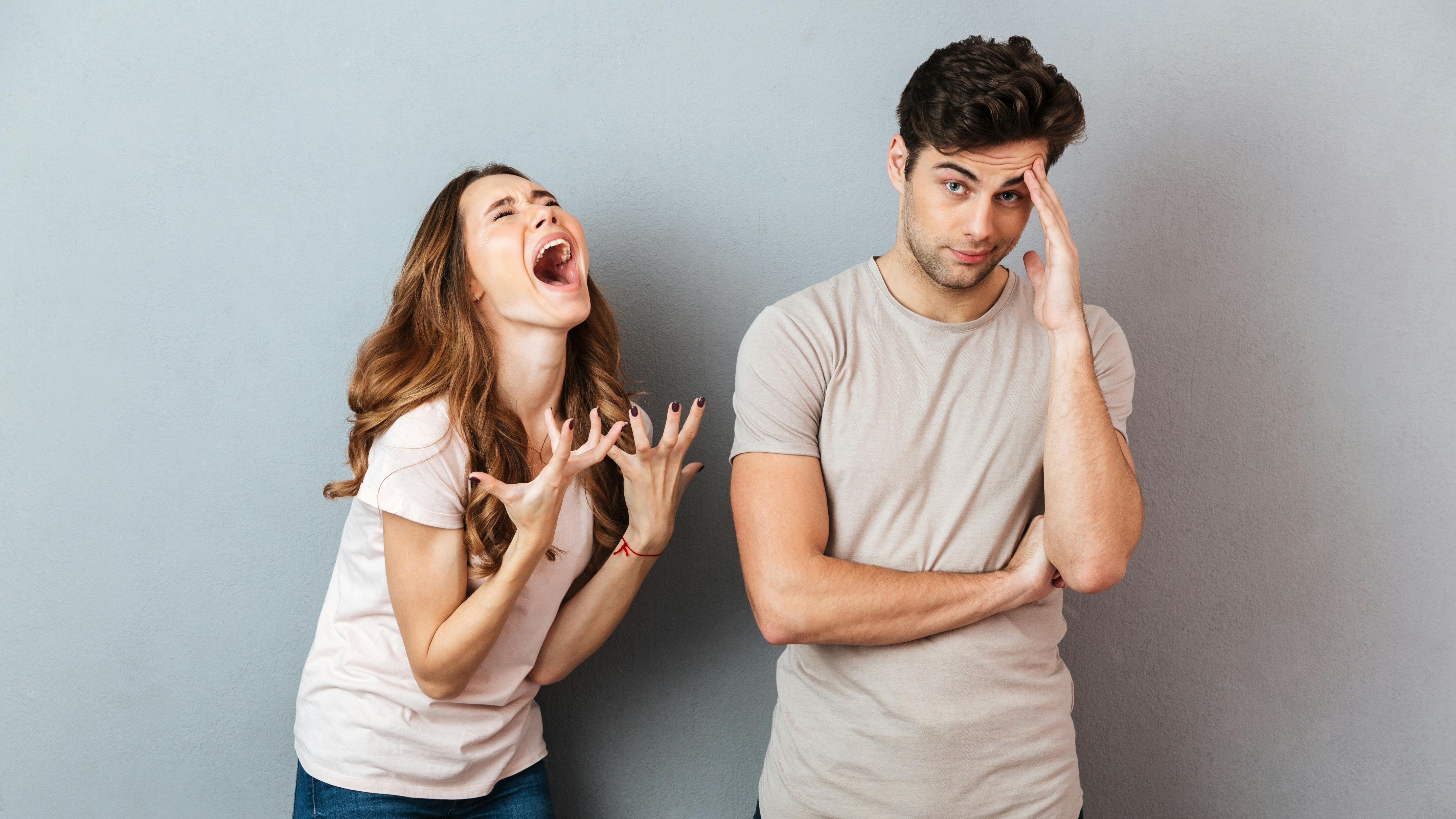 Portrait of a upset young couple having an argument and gesturing over gray wall