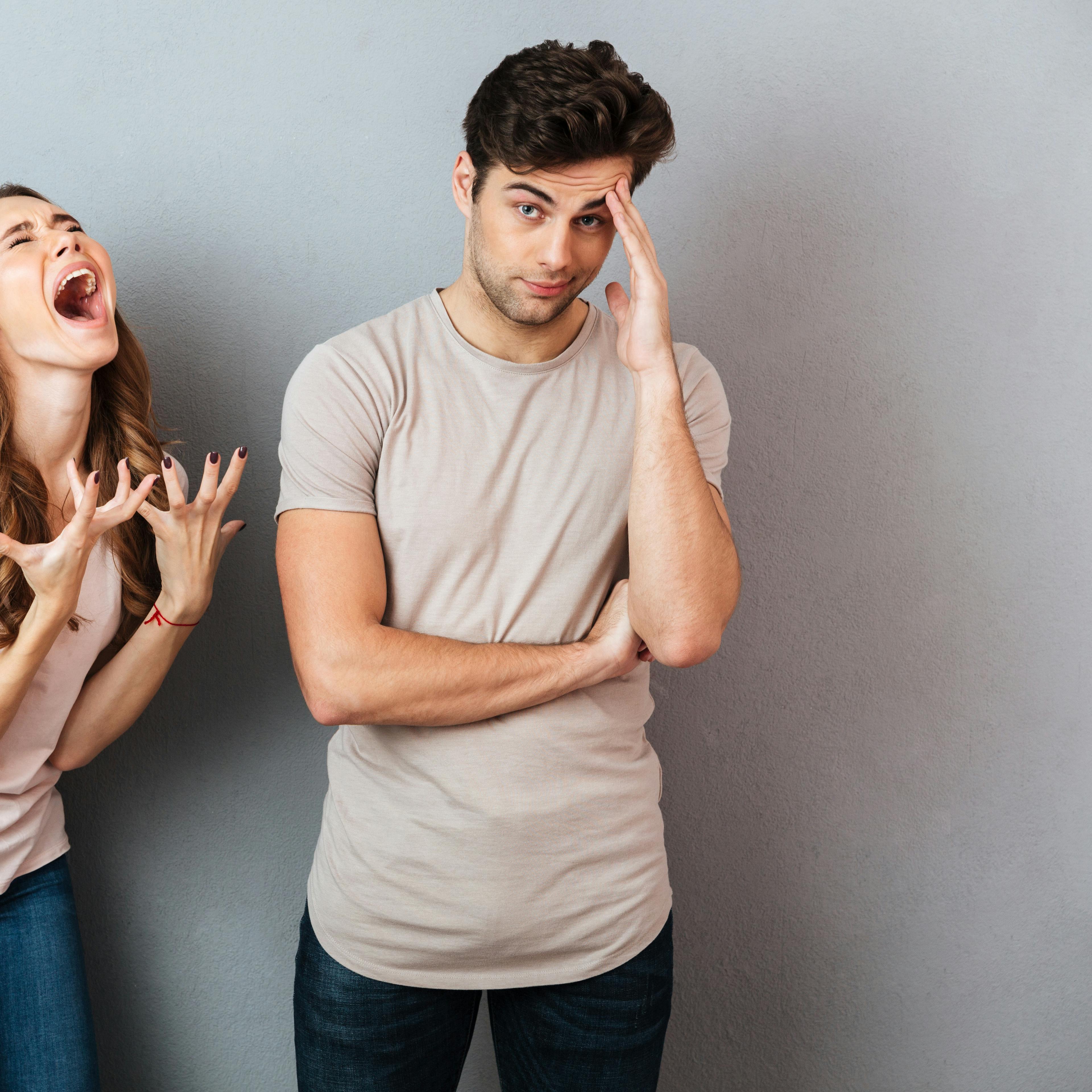 Portrait of a upset young couple having an argument and gesturing over gray wall