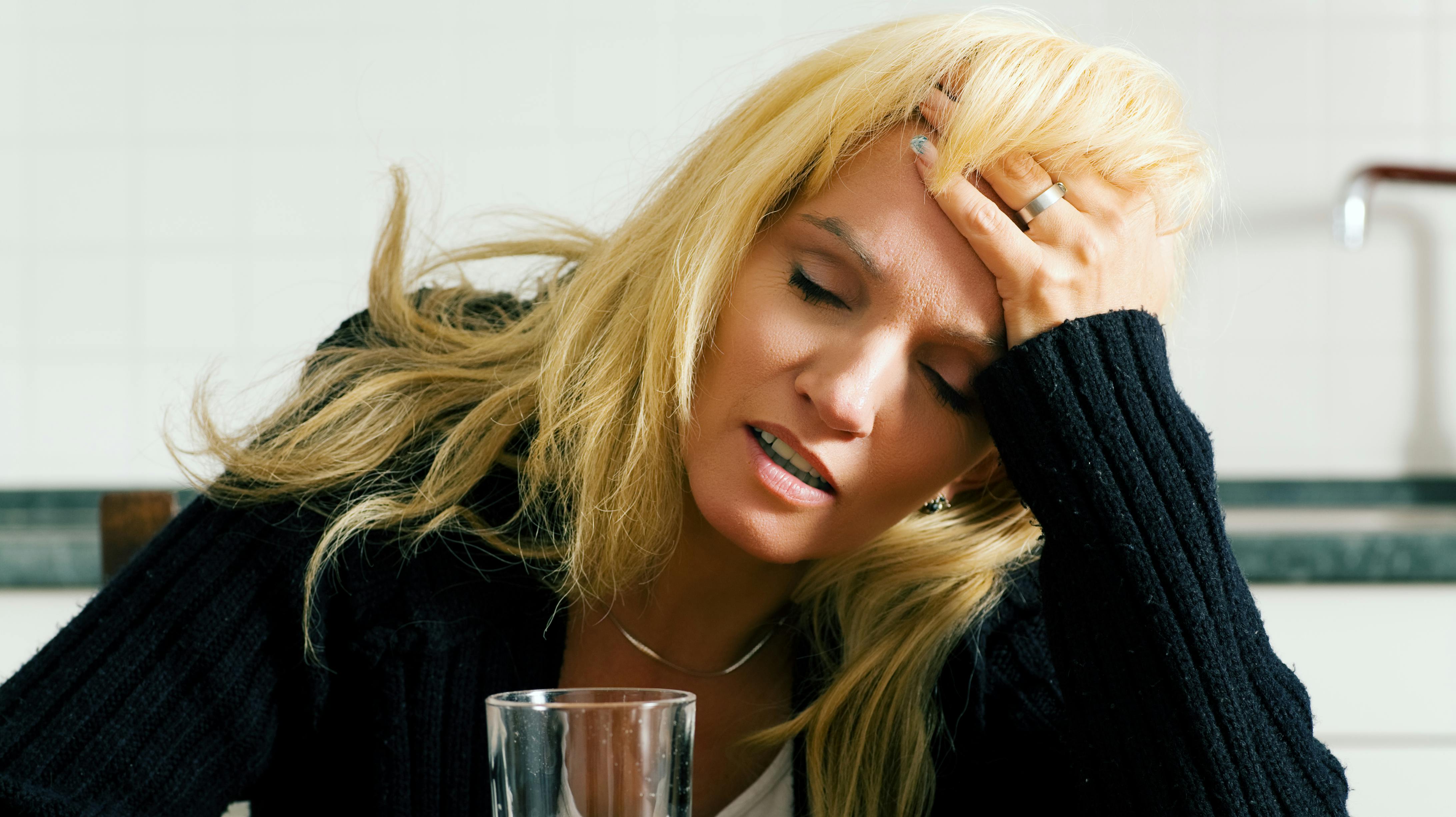Very depressed, sad or grumpy looking woman having headache with a glass of water (presumably wit a painkiller in the water)