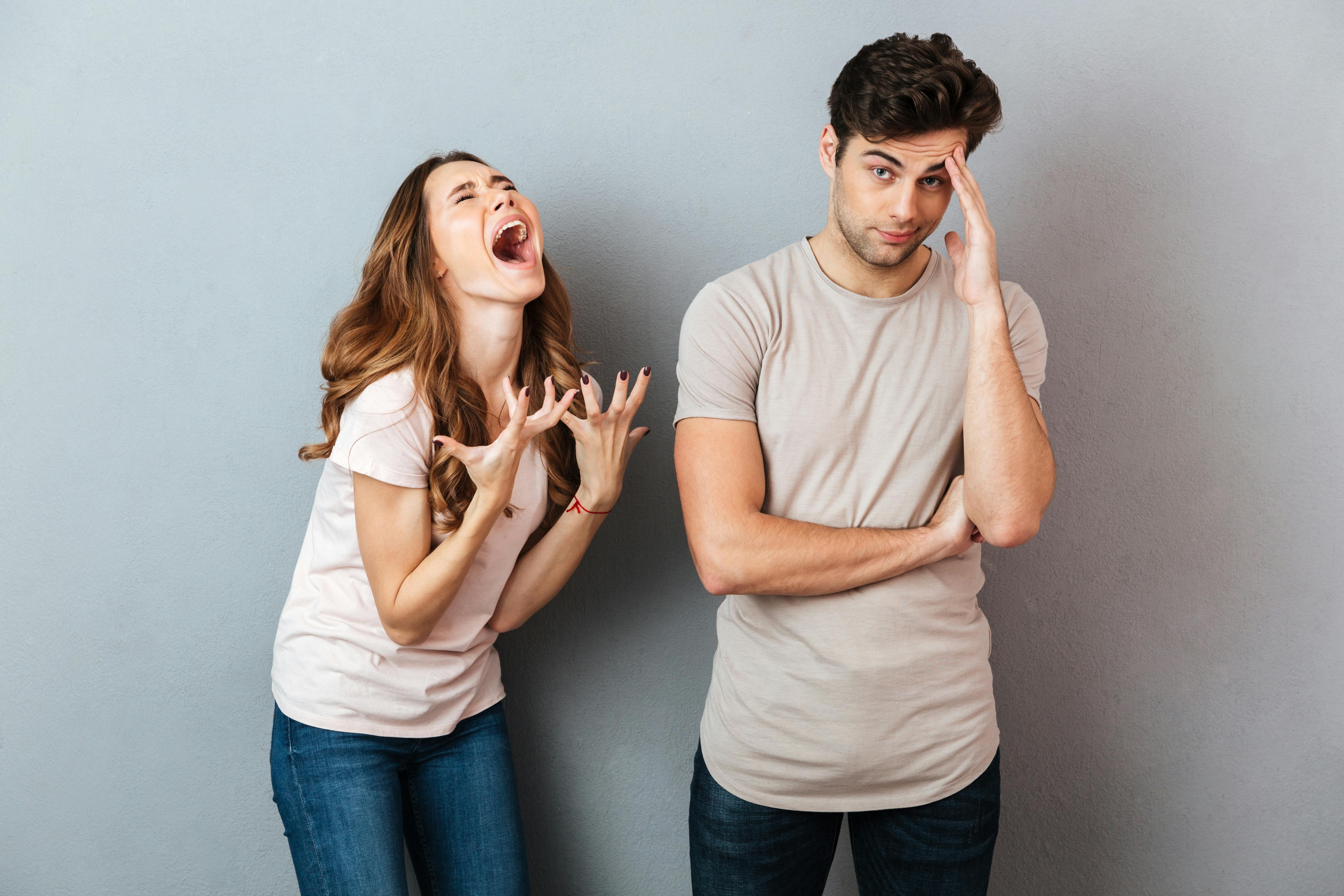 Portrait of a upset young couple having an argument and gesturing over gray wall