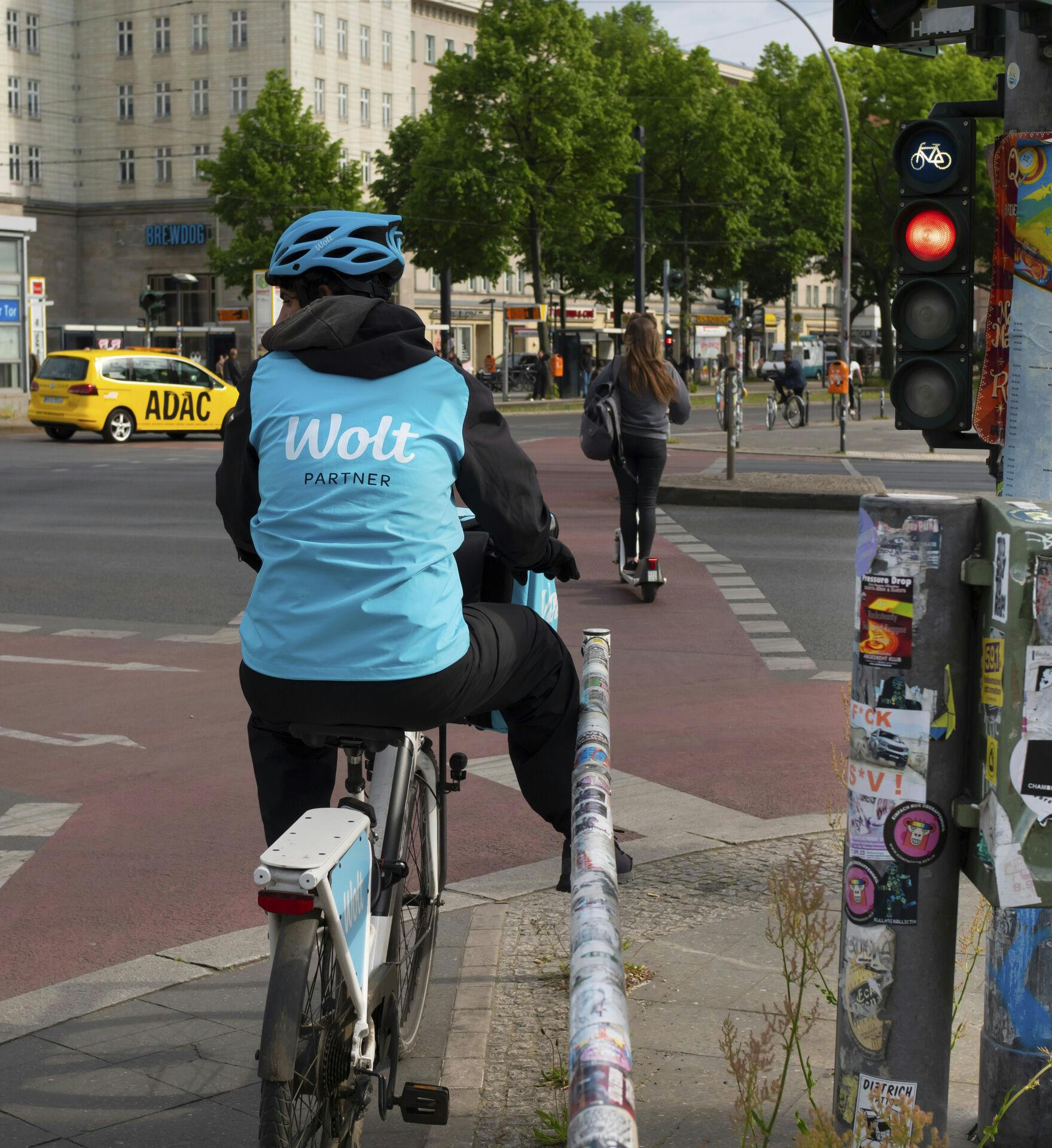 18 May 2023, Berlin: 18.05.2023, Berlin. A messenger from the delivery service Wolt stands with his bicycle in front of a red light in the Friedrichshain district. Wolt is a company from Finland. Photo by: Wolfram Steinberg/picture-alliance/dpa/AP Images