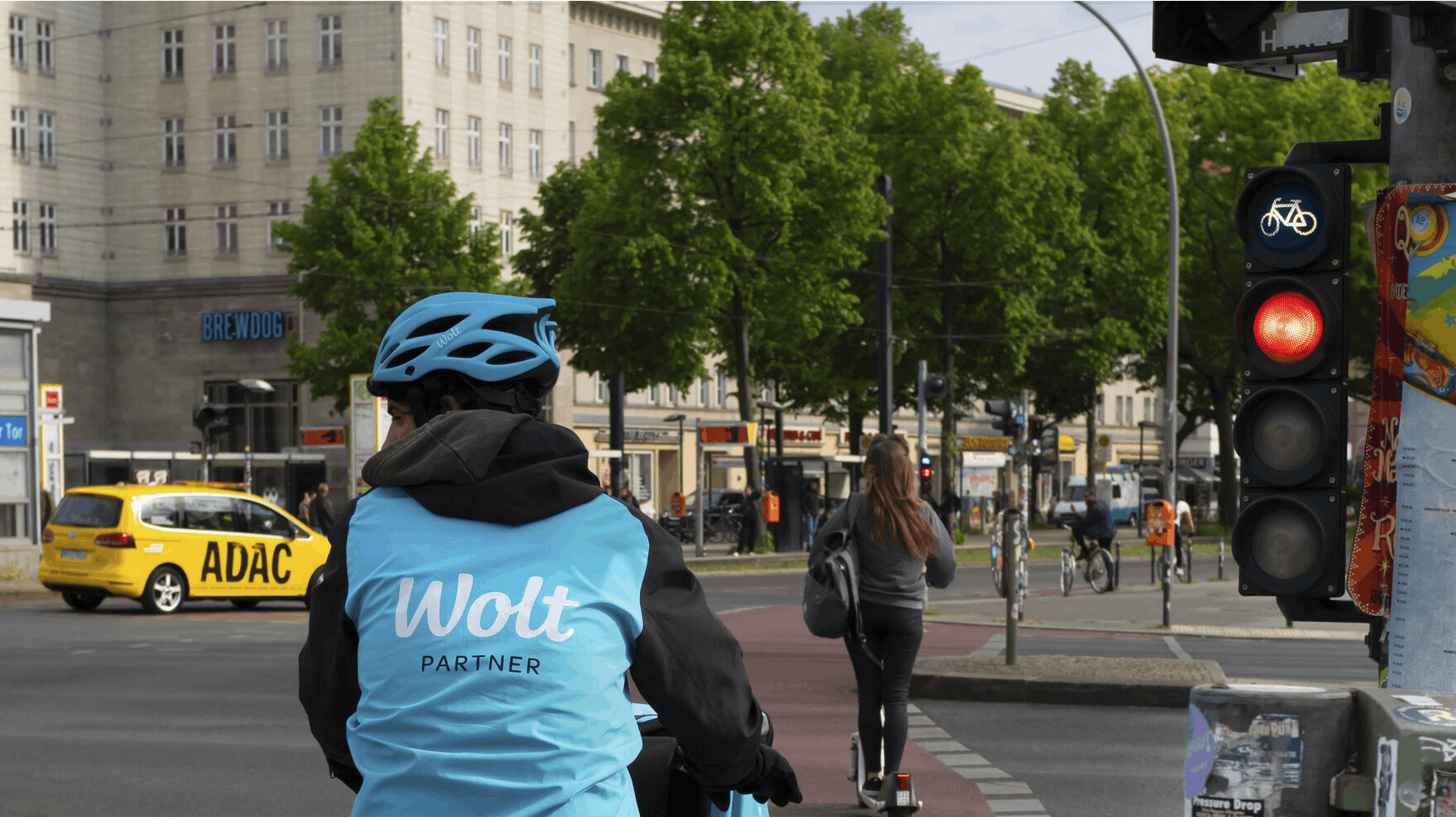 18 May 2023, Berlin: 18.05.2023, Berlin. A messenger from the delivery service Wolt stands with his bicycle in front of a red light in the Friedrichshain district. Wolt is a company from Finland. Photo by: Wolfram Steinberg/picture-alliance/dpa/AP Images