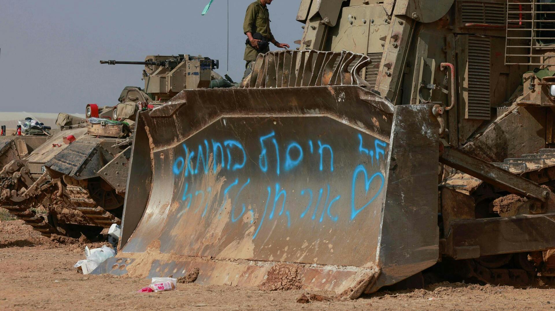 Israelske soldater og militærkøretøjer holder søndag klar ved grænsen til Gazastriben til at rykke ind og støtte den igangværende offensiv. Med blå skrift på bulldozerens grab står: "Vores mission er at ødelægge Hamas". 