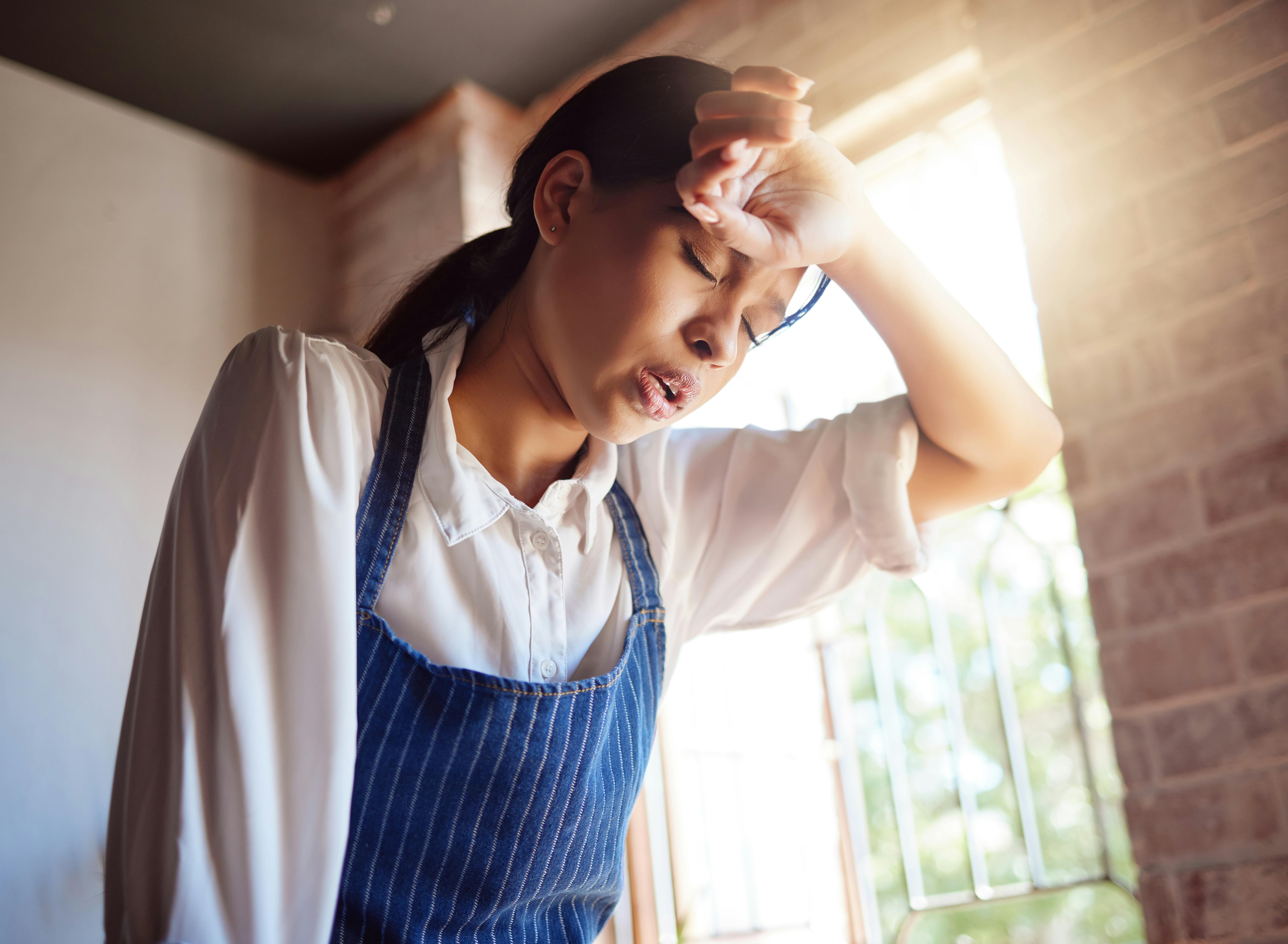 Woman, tired and apron tired from working in cafe, home or cooking job. Girl, chef and cook with headache from cooking burnout or work for service in cafe, kitchen or coffee shop in London.