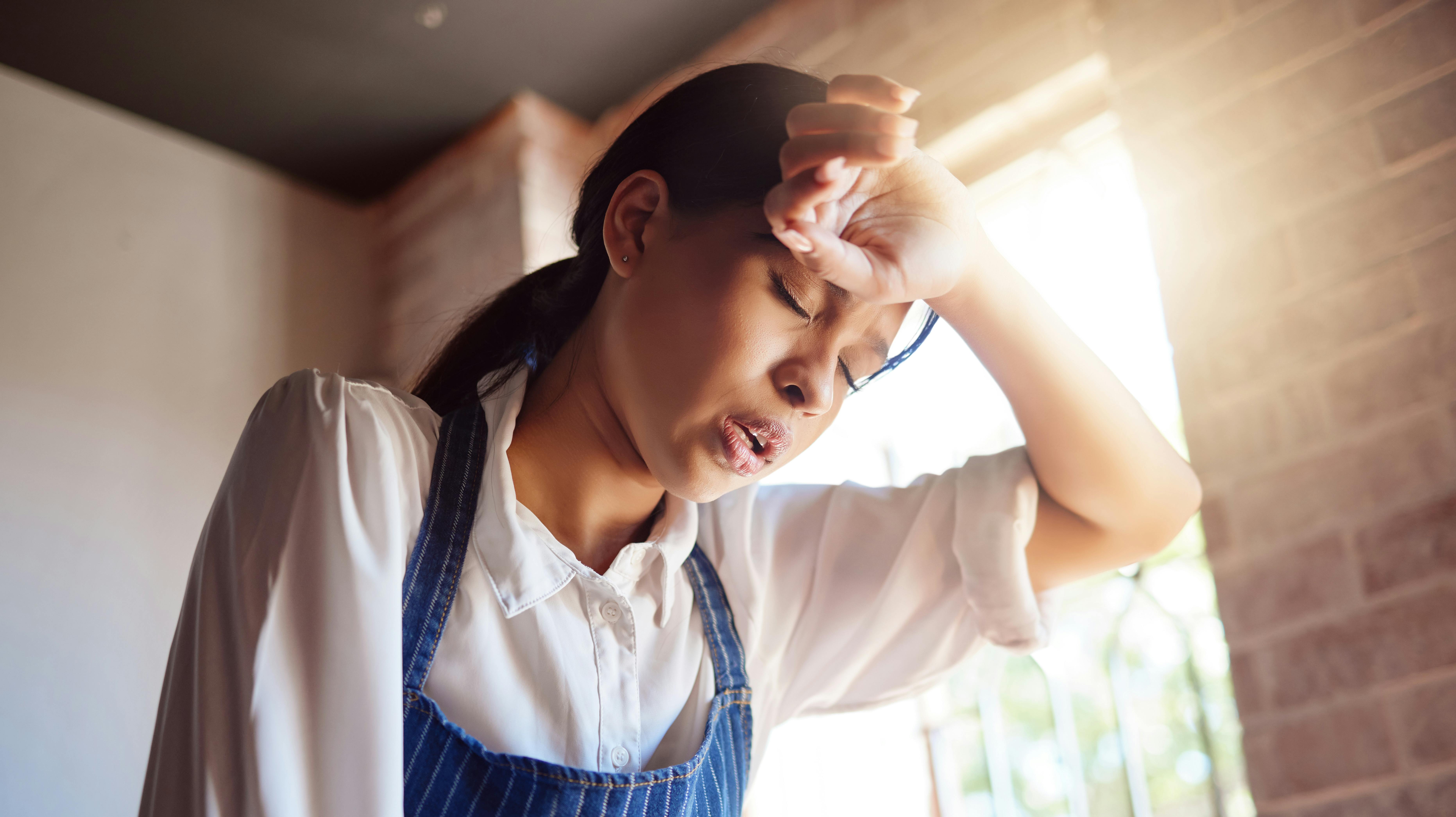 Woman, tired and apron tired from working in cafe, home or cooking job. Girl, chef and cook with headache from cooking burnout or work for service in cafe, kitchen or coffee shop in London.