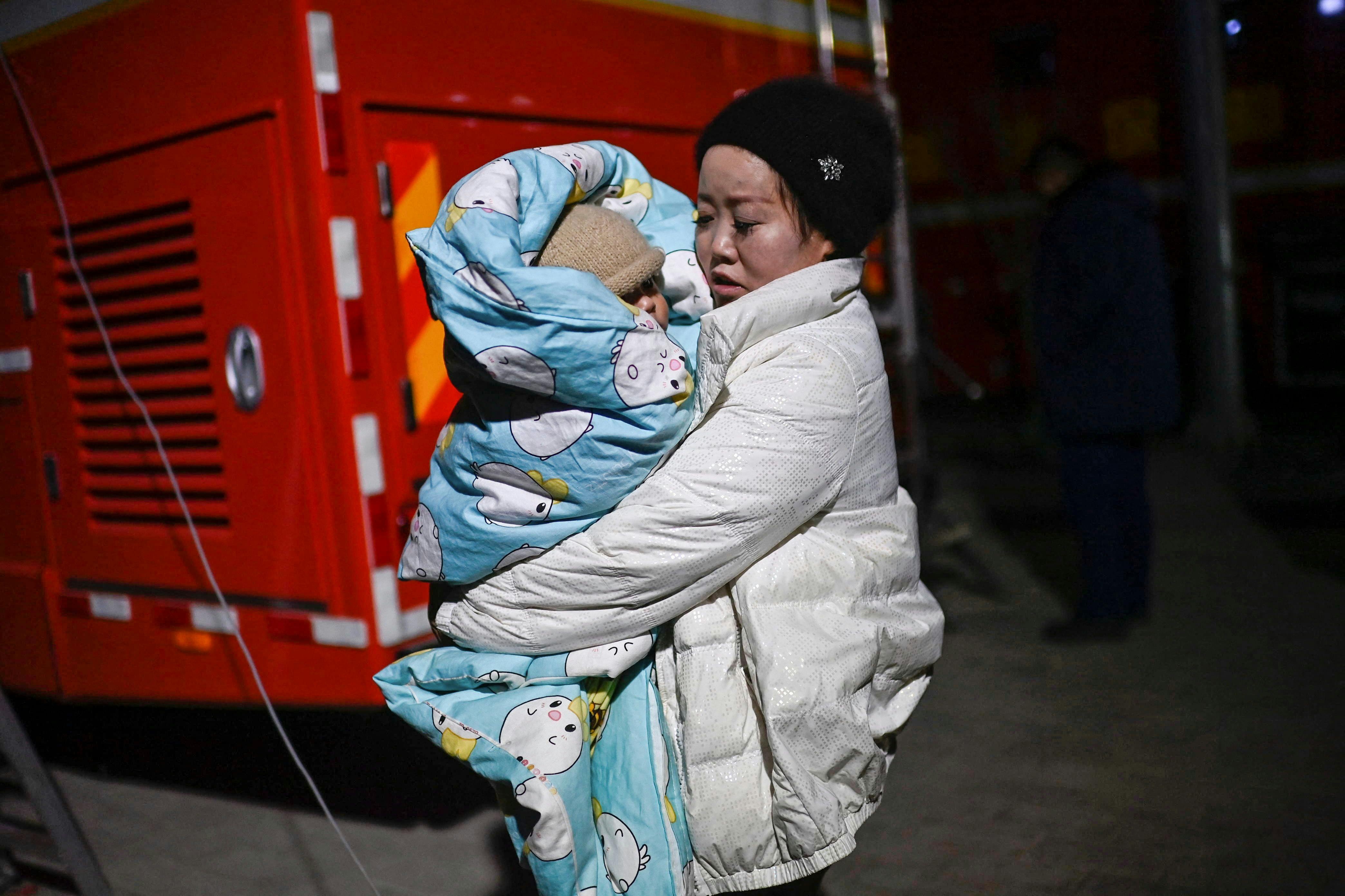 A woman holds a child on a street after an earthquake in Dahejia, Jishishan County in northwest China's Gansu province on December 19, 2023. (Photo by Pedro Pardo / AFP)