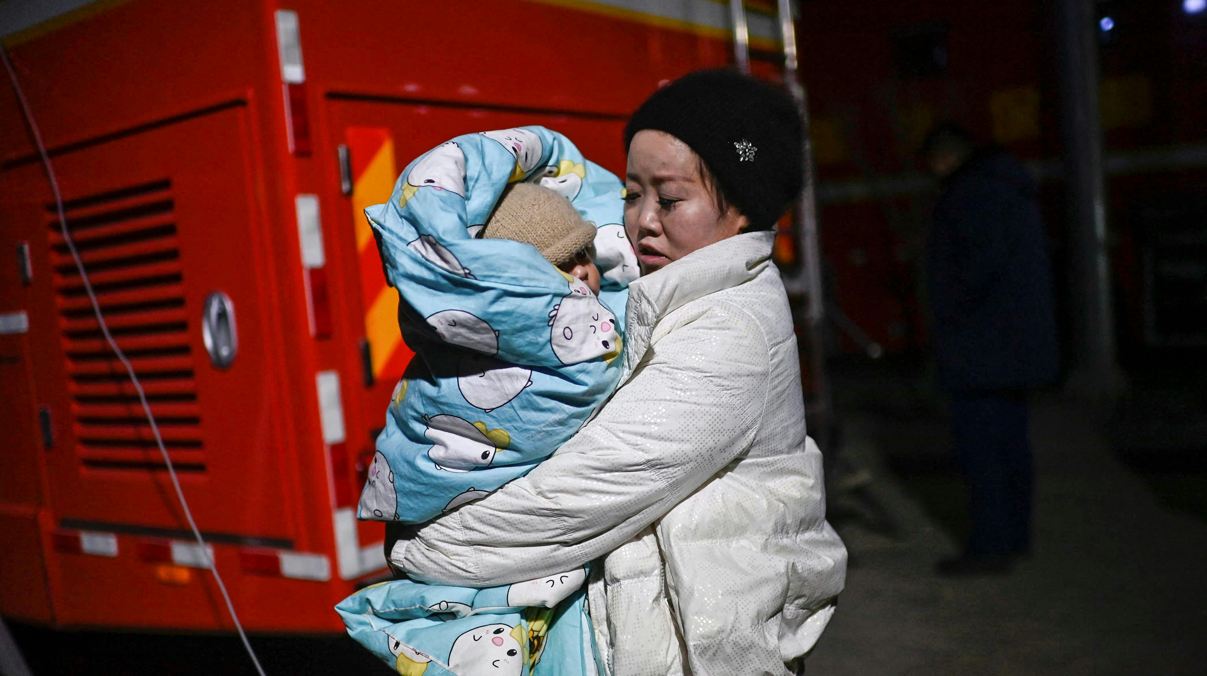 A woman holds a child on a street after an earthquake in Dahejia, Jishishan County in northwest China's Gansu province on December 19, 2023. (Photo by Pedro Pardo / AFP)