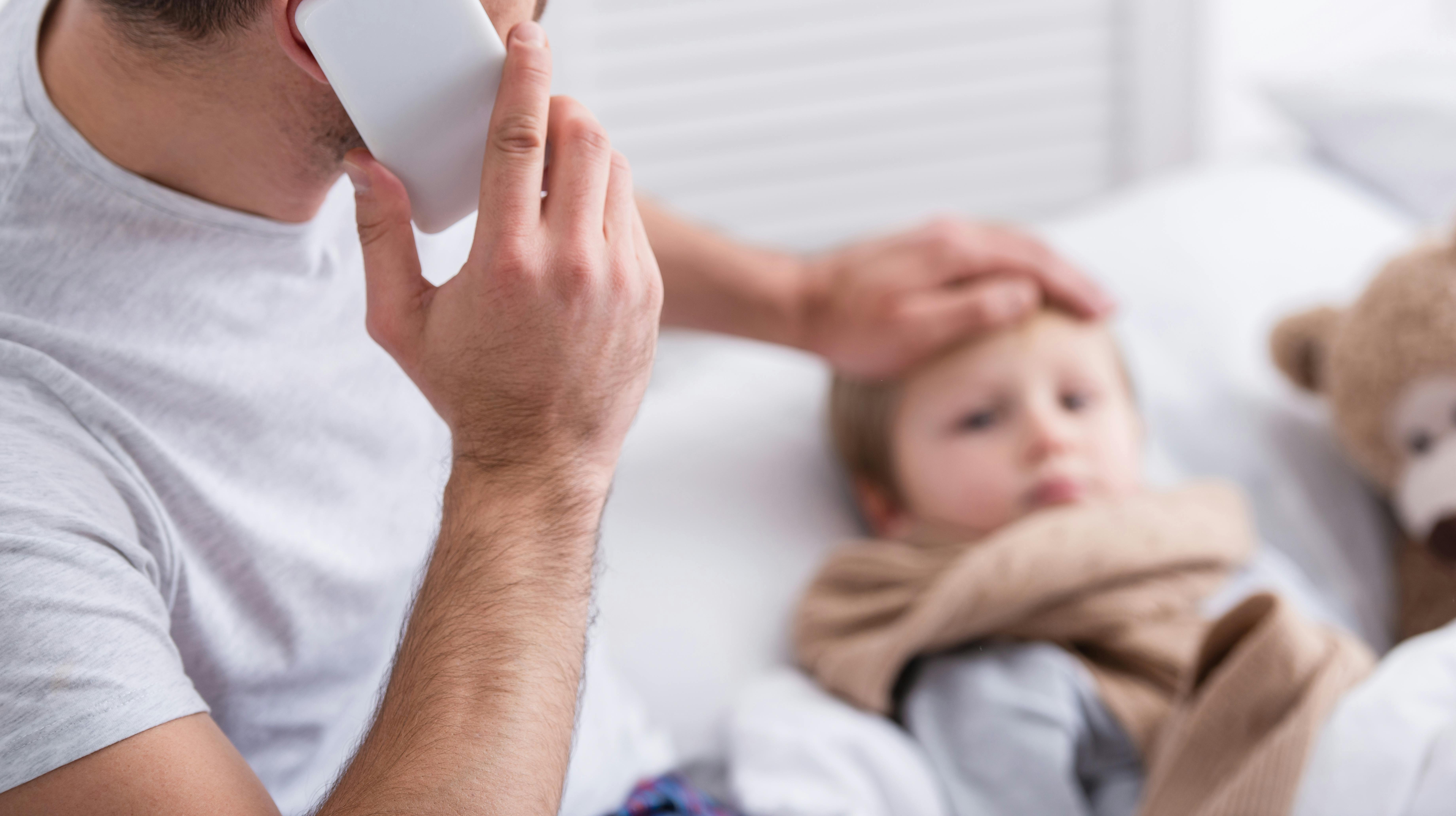 selective focus of father talking by smartphone and touching sick son forehead in bedroom