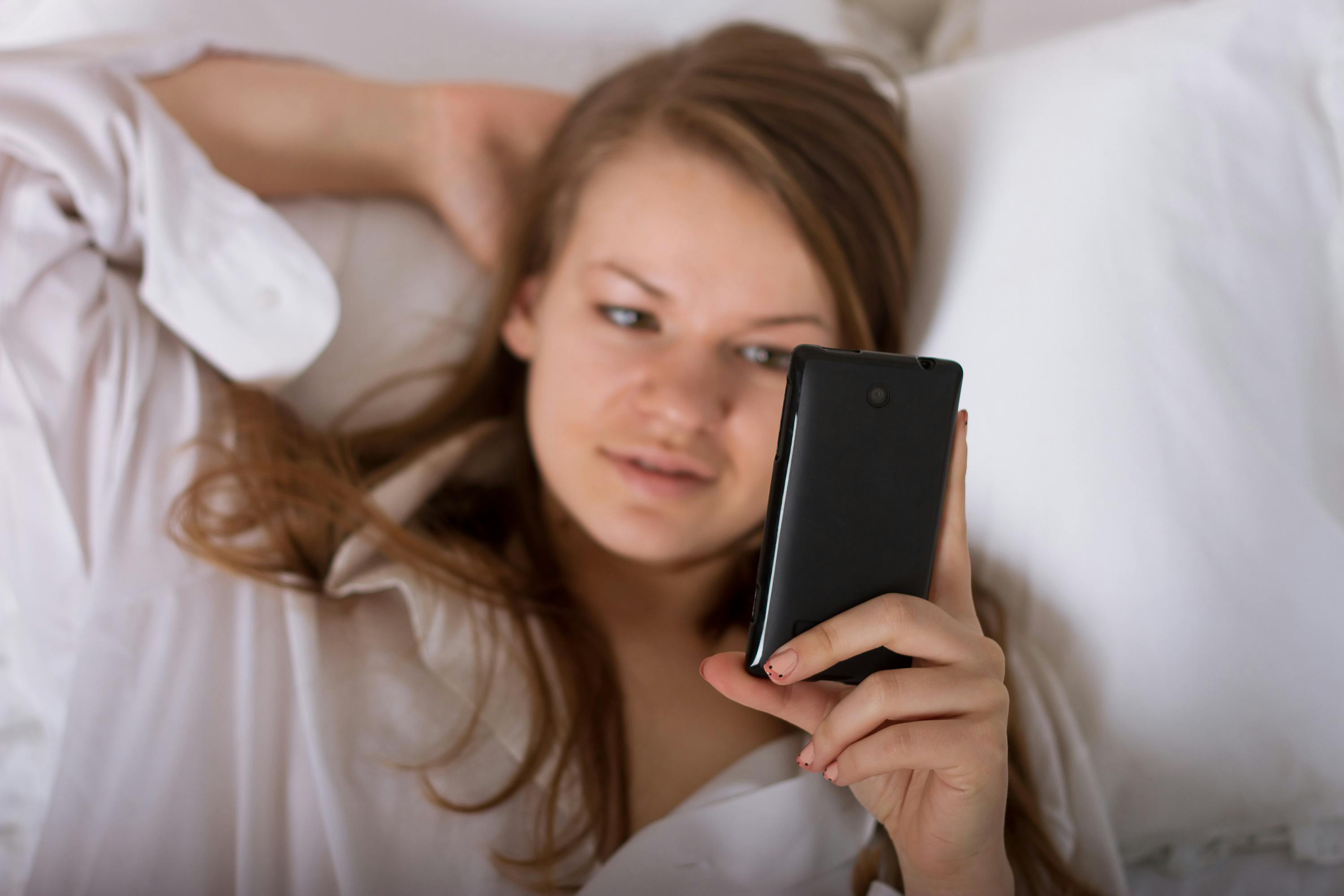 Beautiful woman sending a text with a mobile phone in bed
