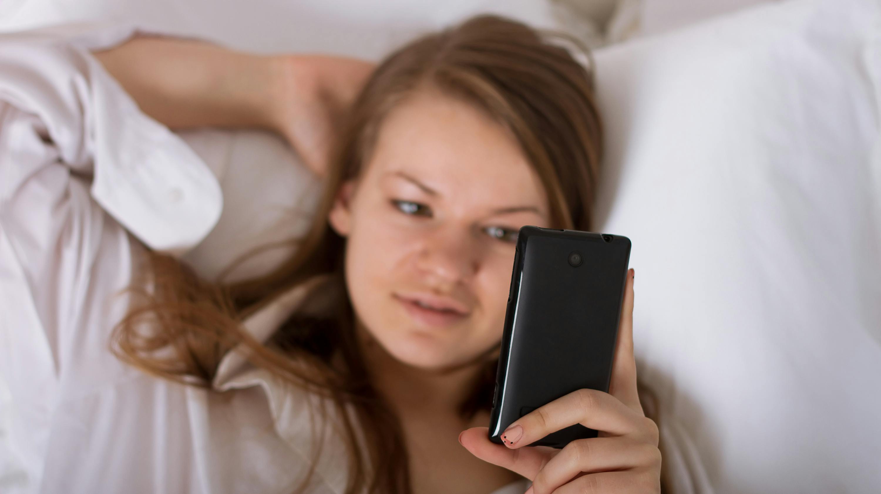 Beautiful woman sending a text with a mobile phone in bed