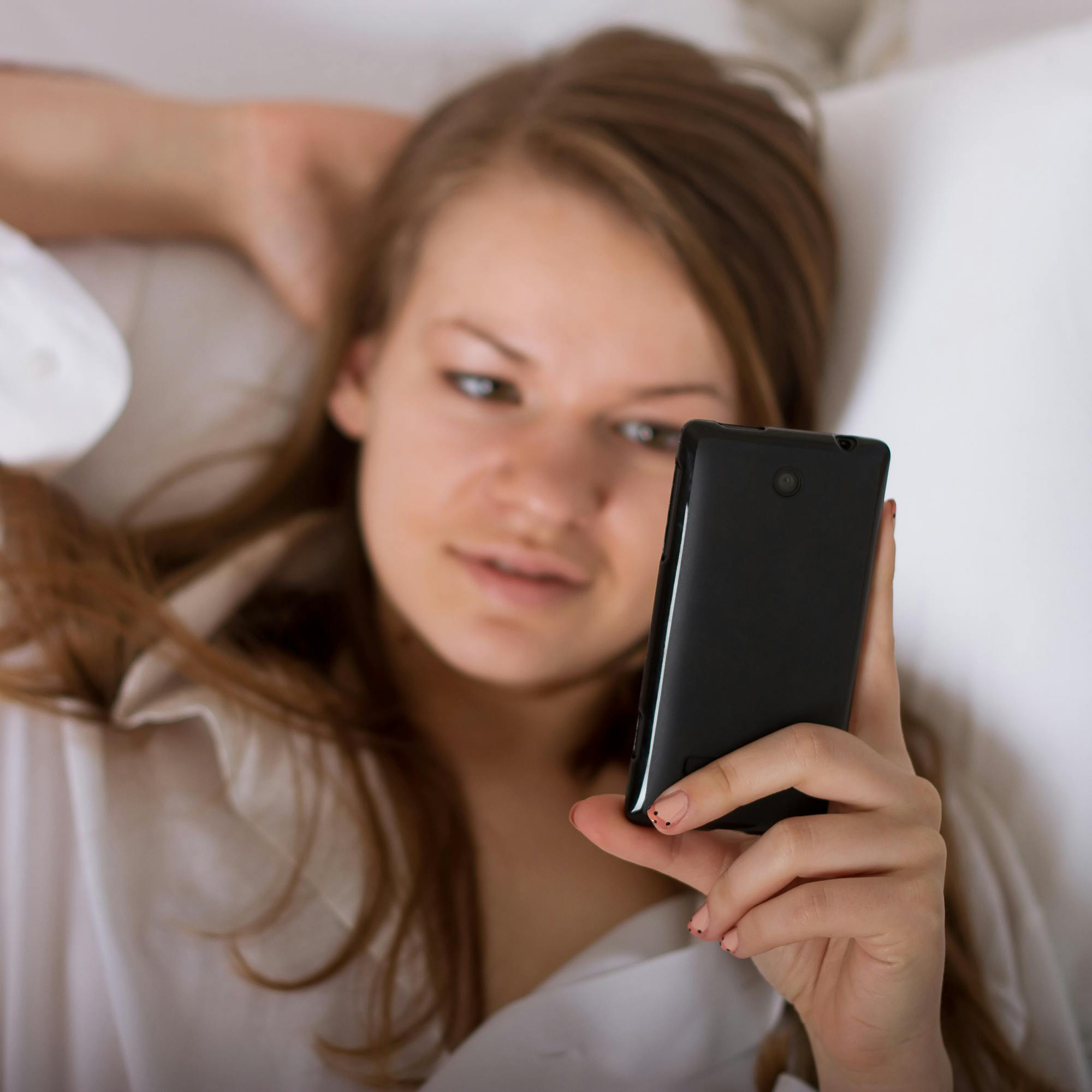 Beautiful woman sending a text with a mobile phone in bed