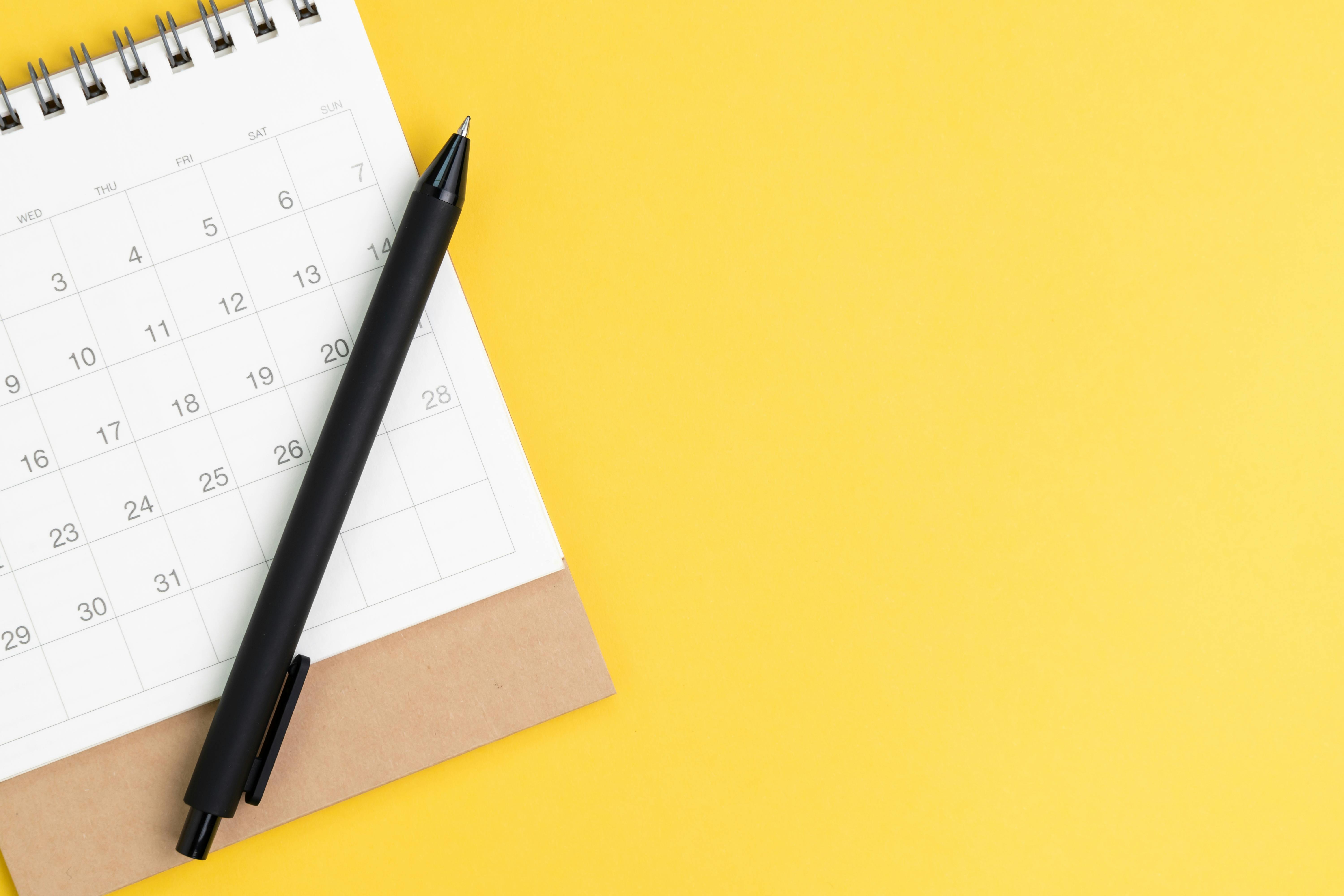 Black pen on desktop calendar in flat lay or top view on yellow background with copy space using as writing plan, circle on important day and event or appointment concept.
