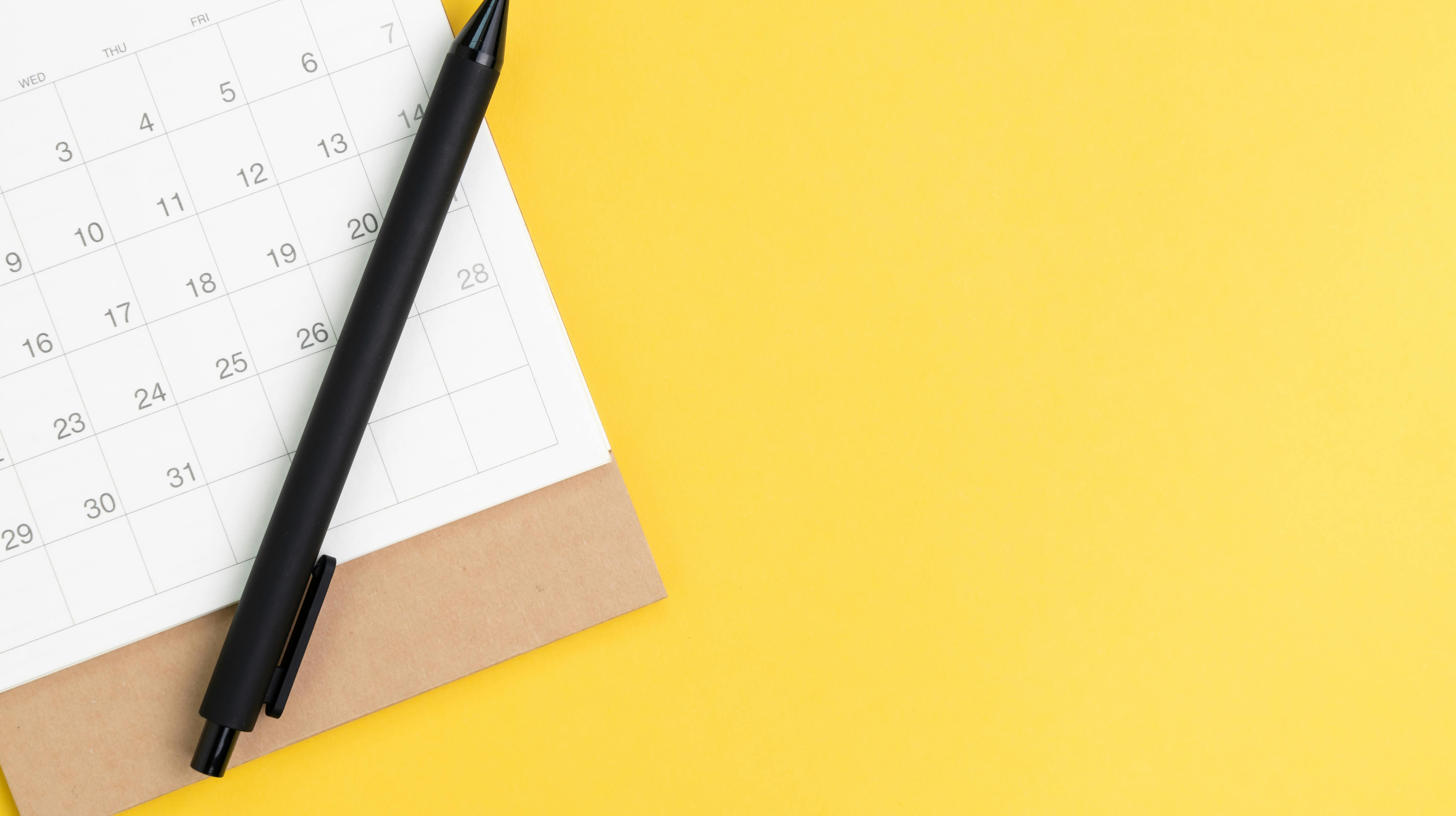 Black pen on desktop calendar in flat lay or top view on yellow background with copy space using as writing plan, circle on important day and event or appointment concept.