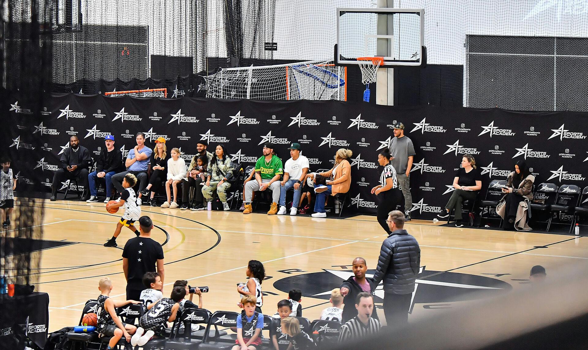 Kanye West yderst til venstre og Kim Kardashian på sin telefon yderst til højre under sønnens basketkamp.