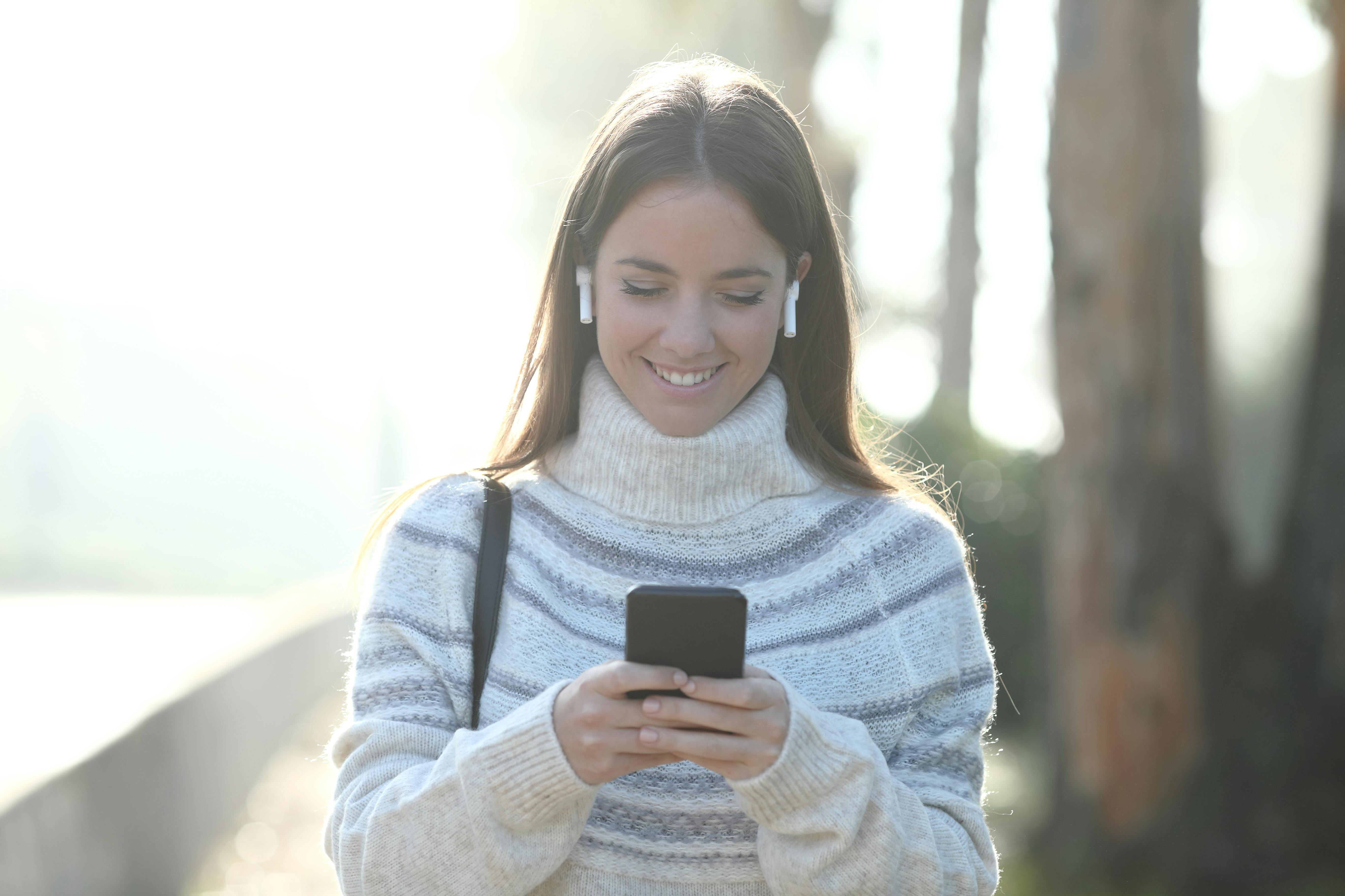 Front view portrait of a happy woman in winter using mobile phone walking in a park