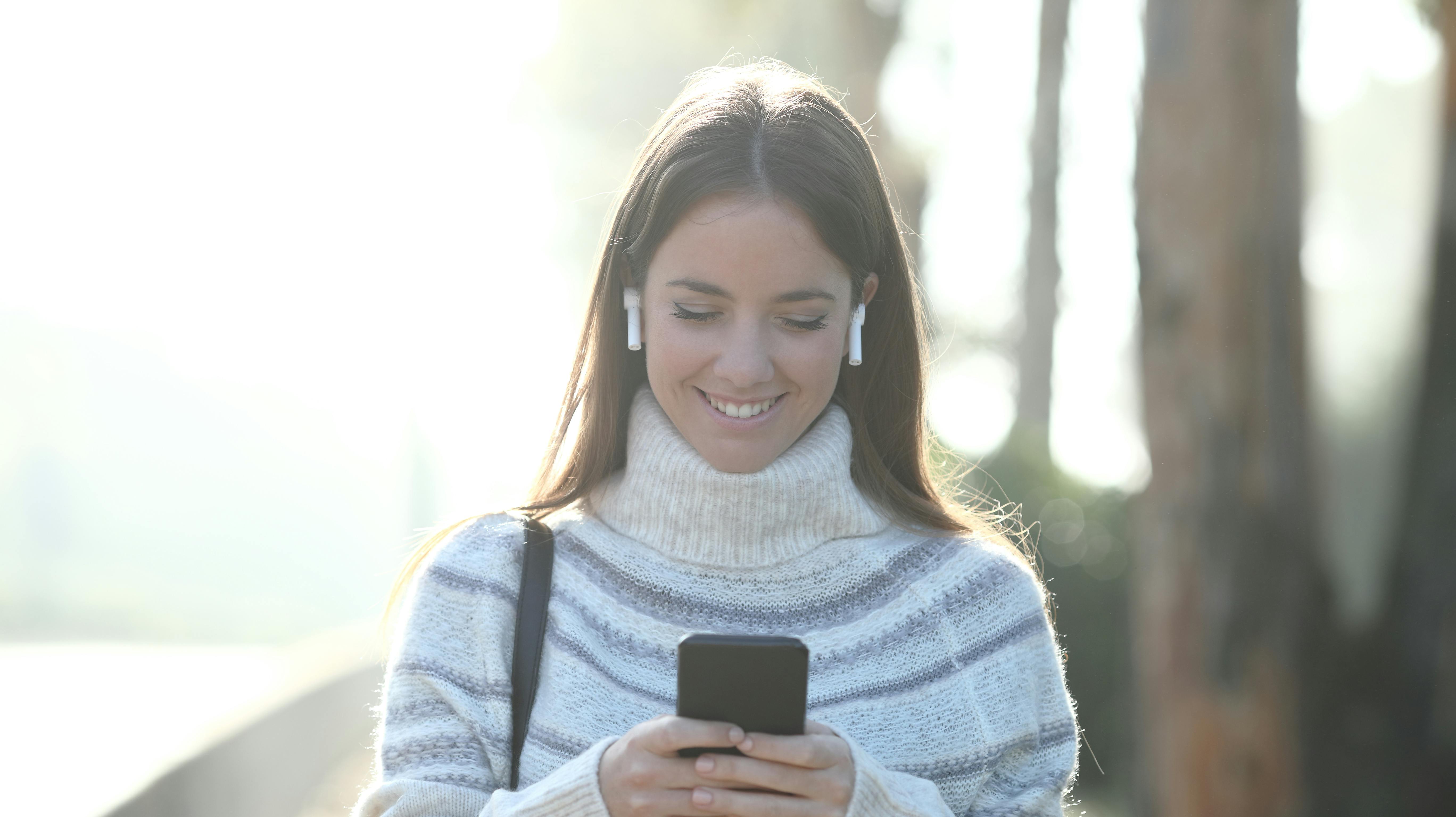 Front view portrait of a happy woman in winter using mobile phone walking in a park