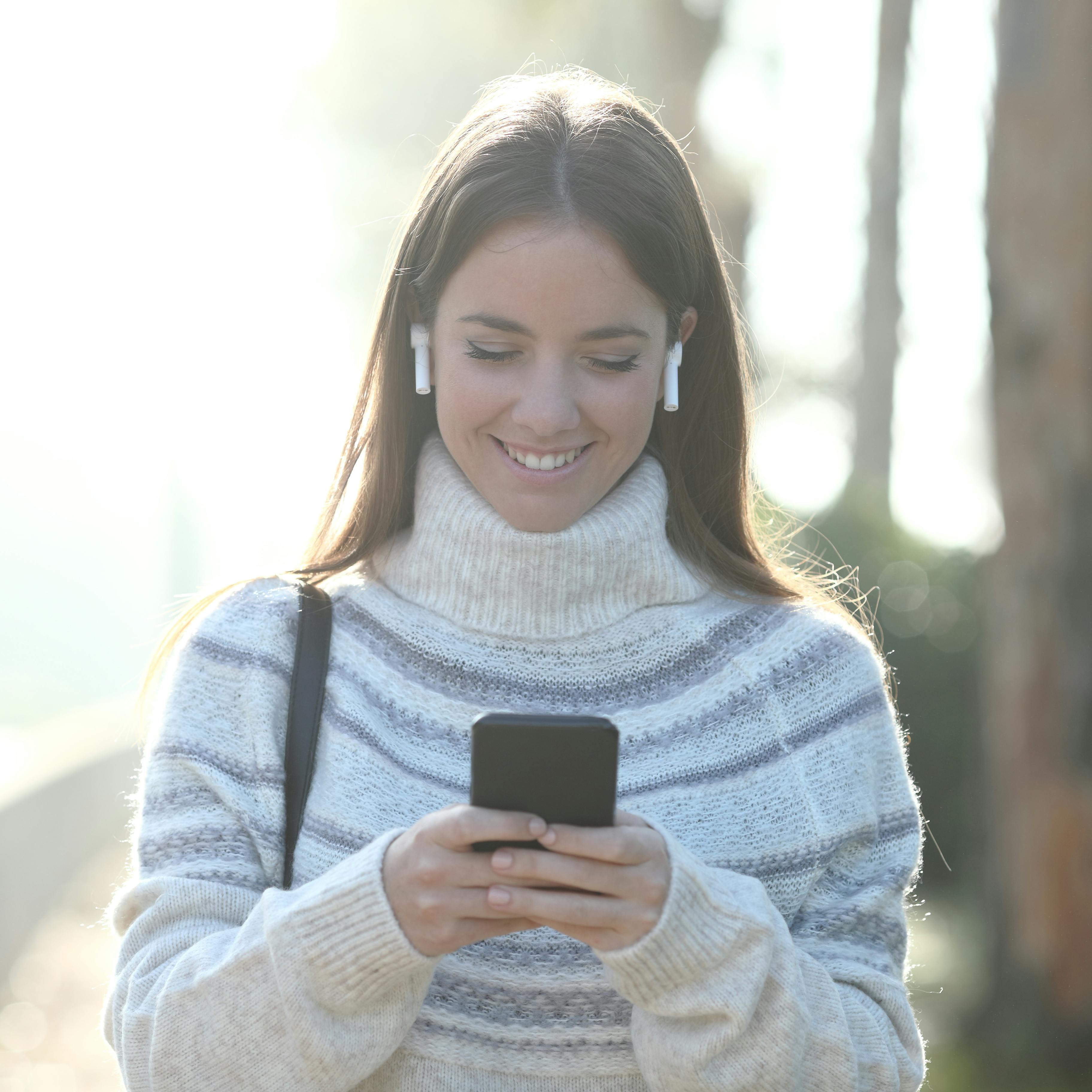 Front view portrait of a happy woman in winter using mobile phone walking in a park