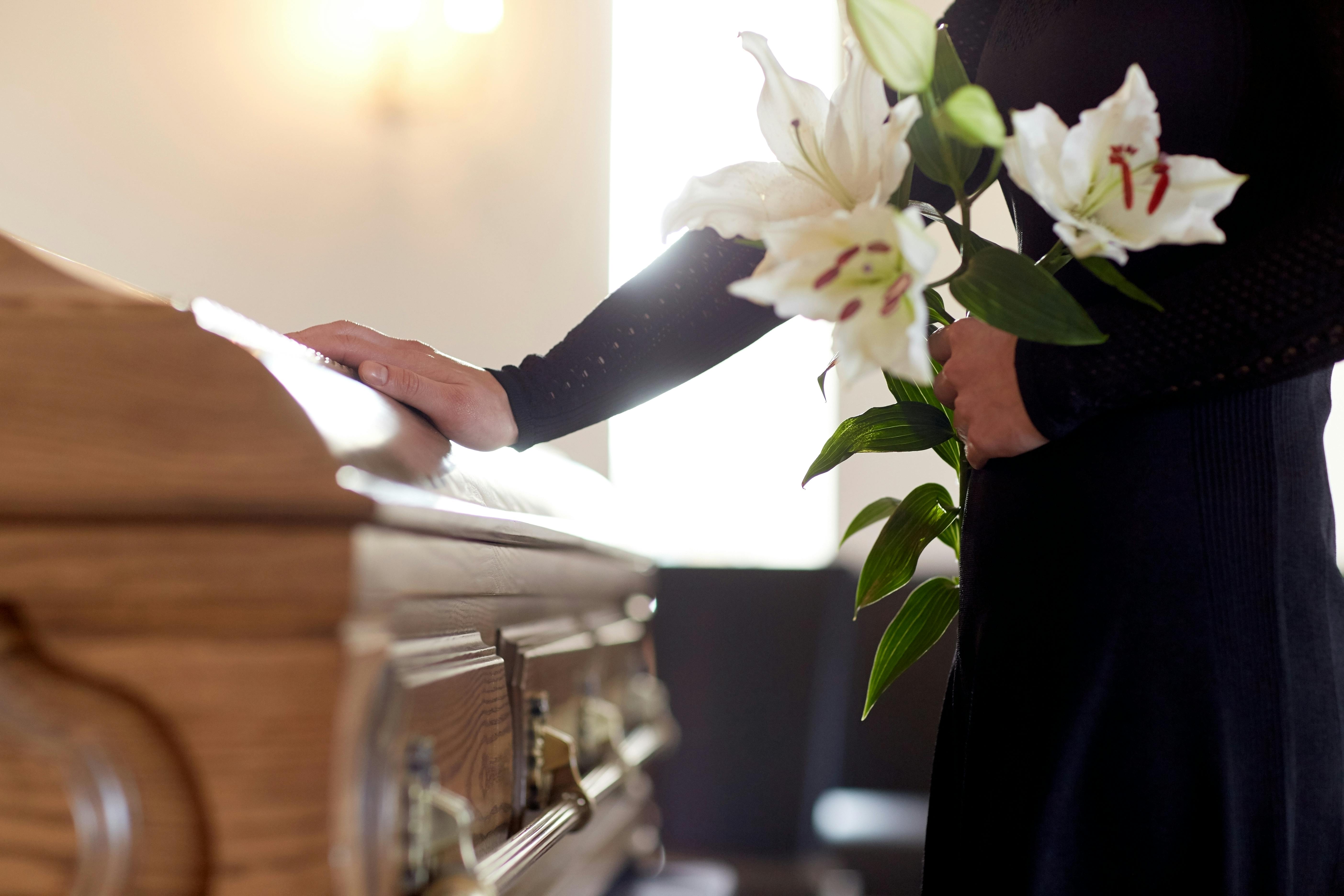 people and mourning concept – woman with white lily flowers and coffin at funeral in church