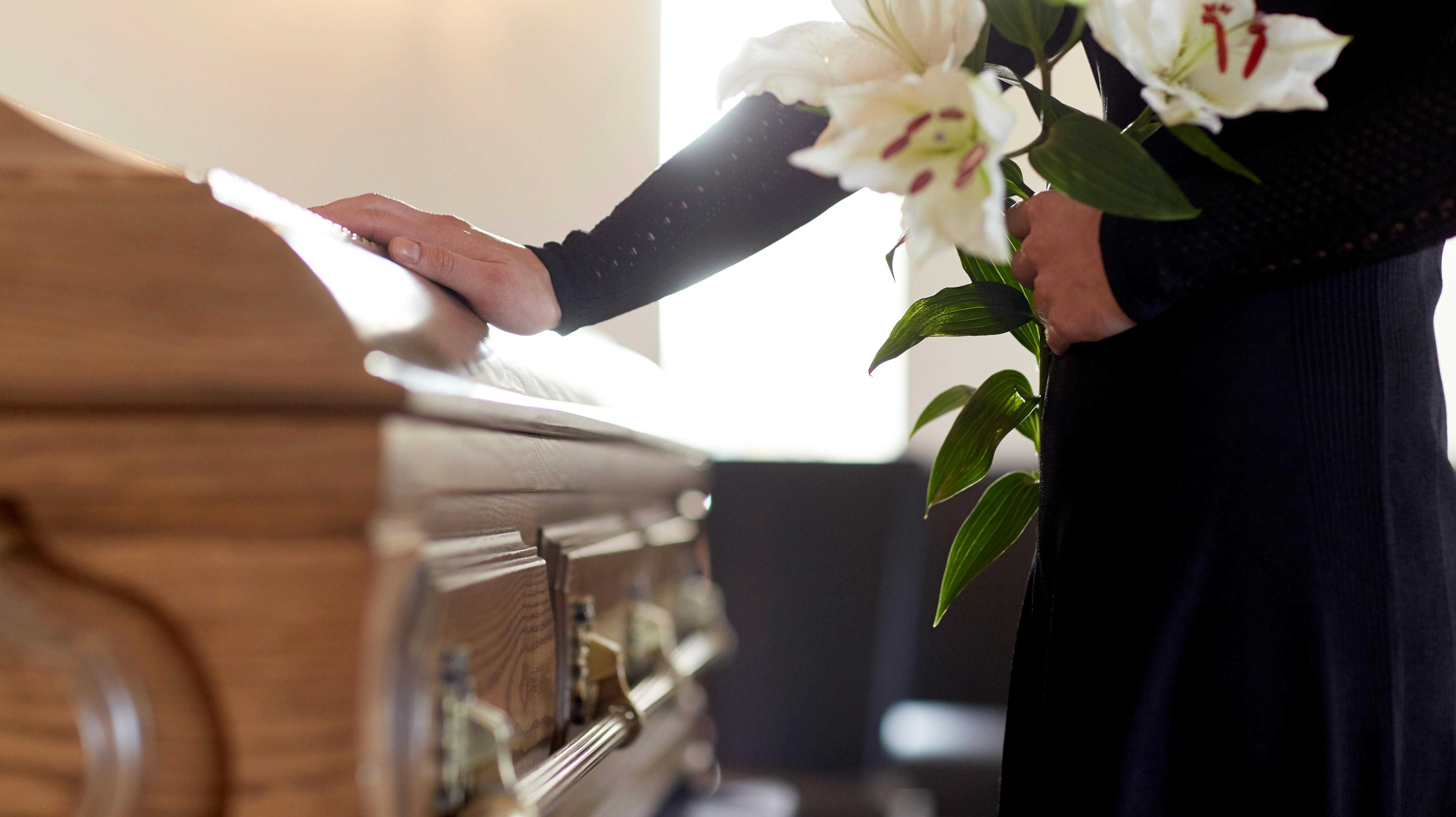 people and mourning concept – woman with white lily flowers and coffin at funeral in church
