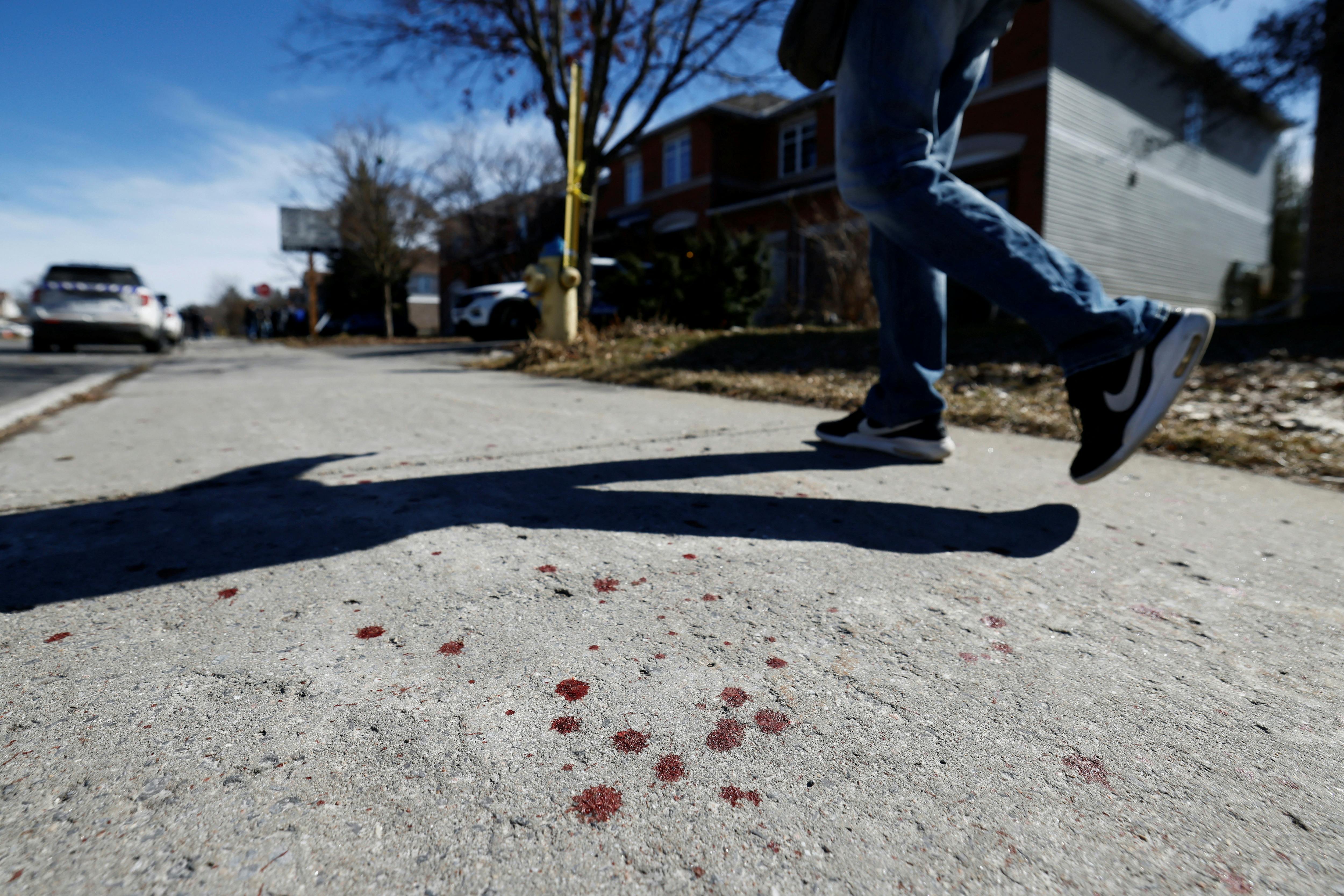 A pedestrian walks past blood splatter on a sidewalk after four children and two adults were found dead inside a nearby house in the Ottawa suburb of Barrhaven, Ontario, Canada March 7, 2024. REUTERS/Blair Gable