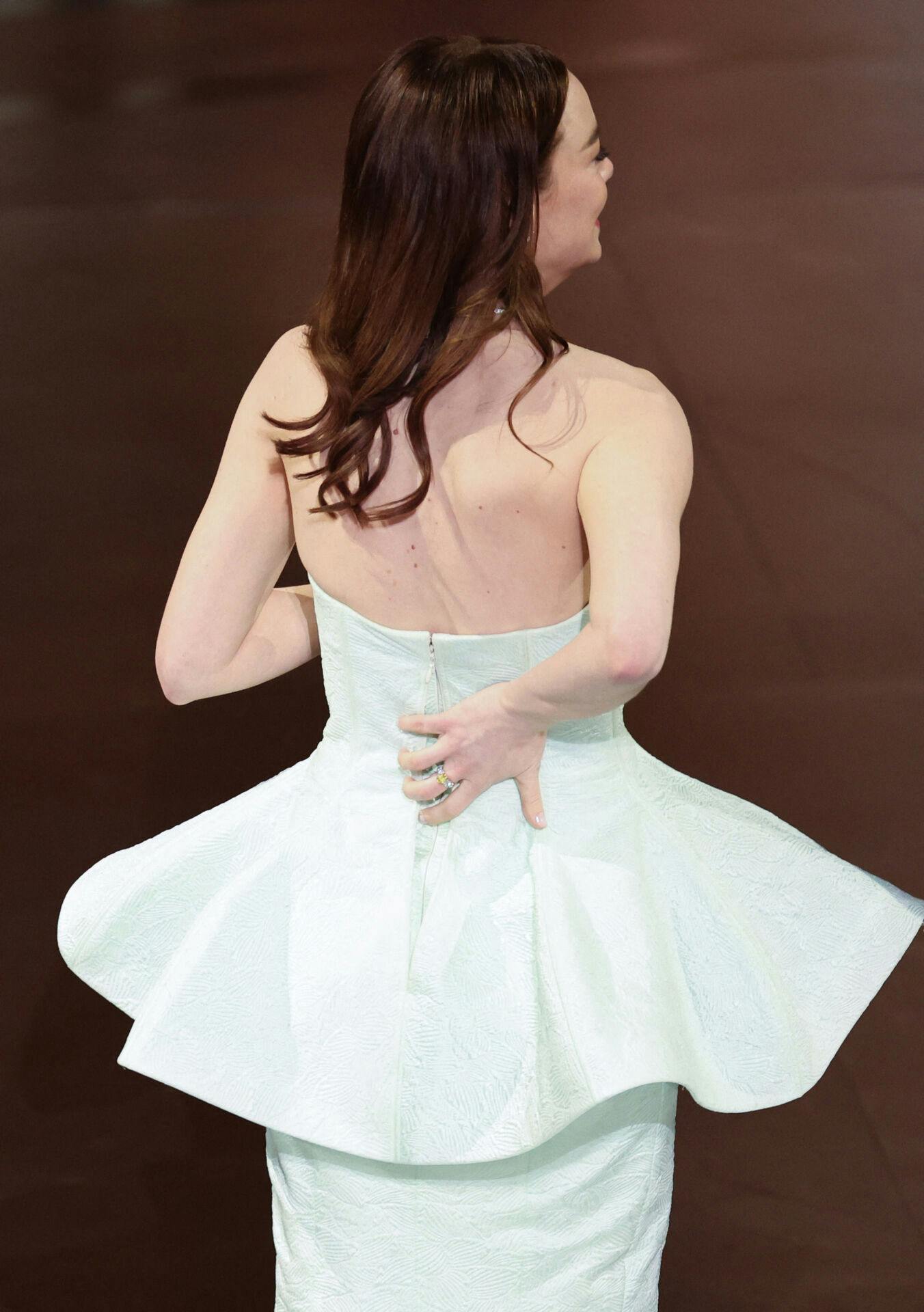 Emma Stone holder sammen på sin kjole, mens hun er på vej op på scenen for at modtage sit livs anden Oscar-statuette.