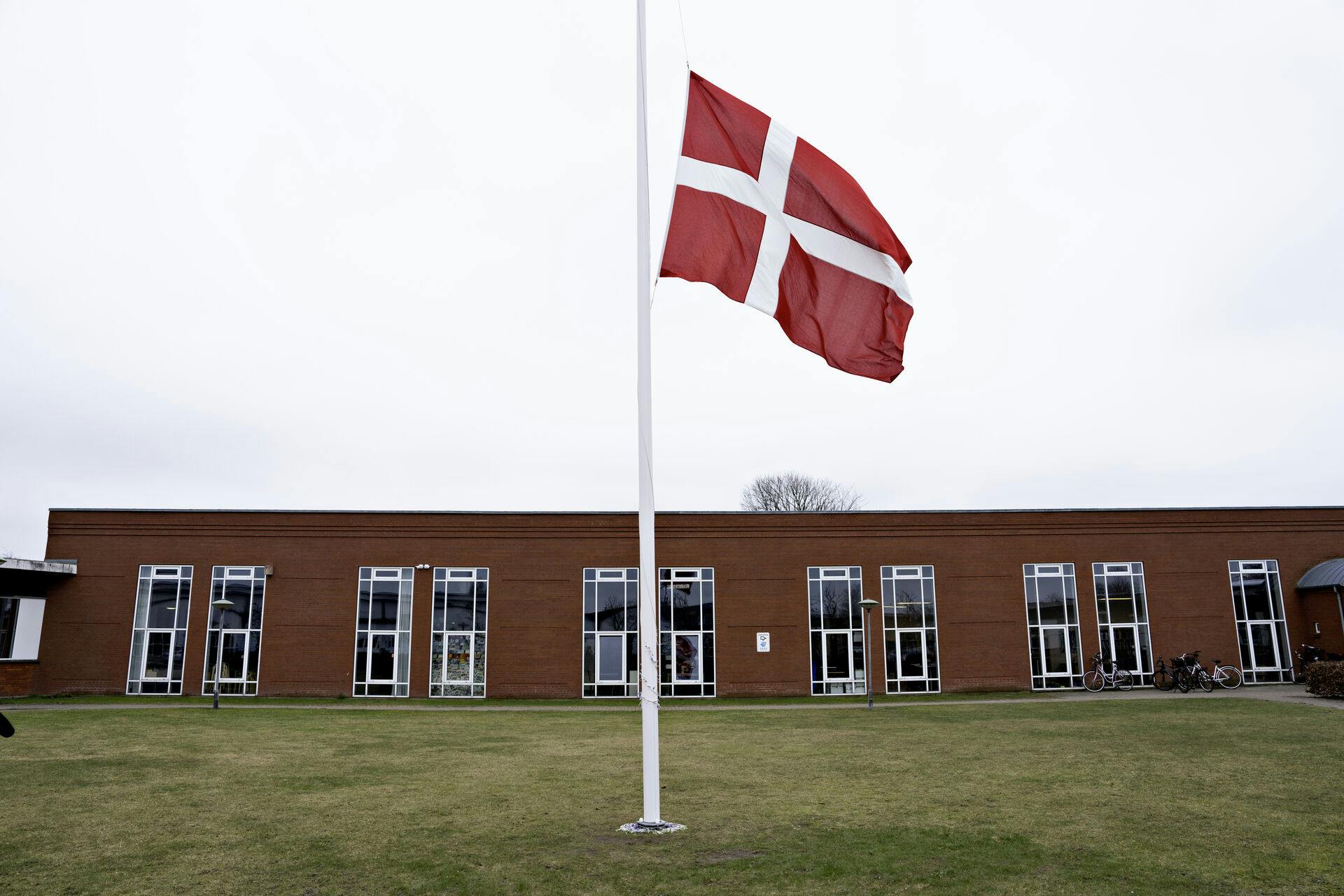 Der flages på halv stang ved Hjallerup Skole i Nordjylland tirsdag den 12. marts 2024. En 17-årig dreng er anholdt i sag om drab på 13-årig pige i Hjallerup, oplyser politiet. Ved foden af flagstamgen ligger blomster. (Foto: Henning Bagger/Ritzau Scanpix)