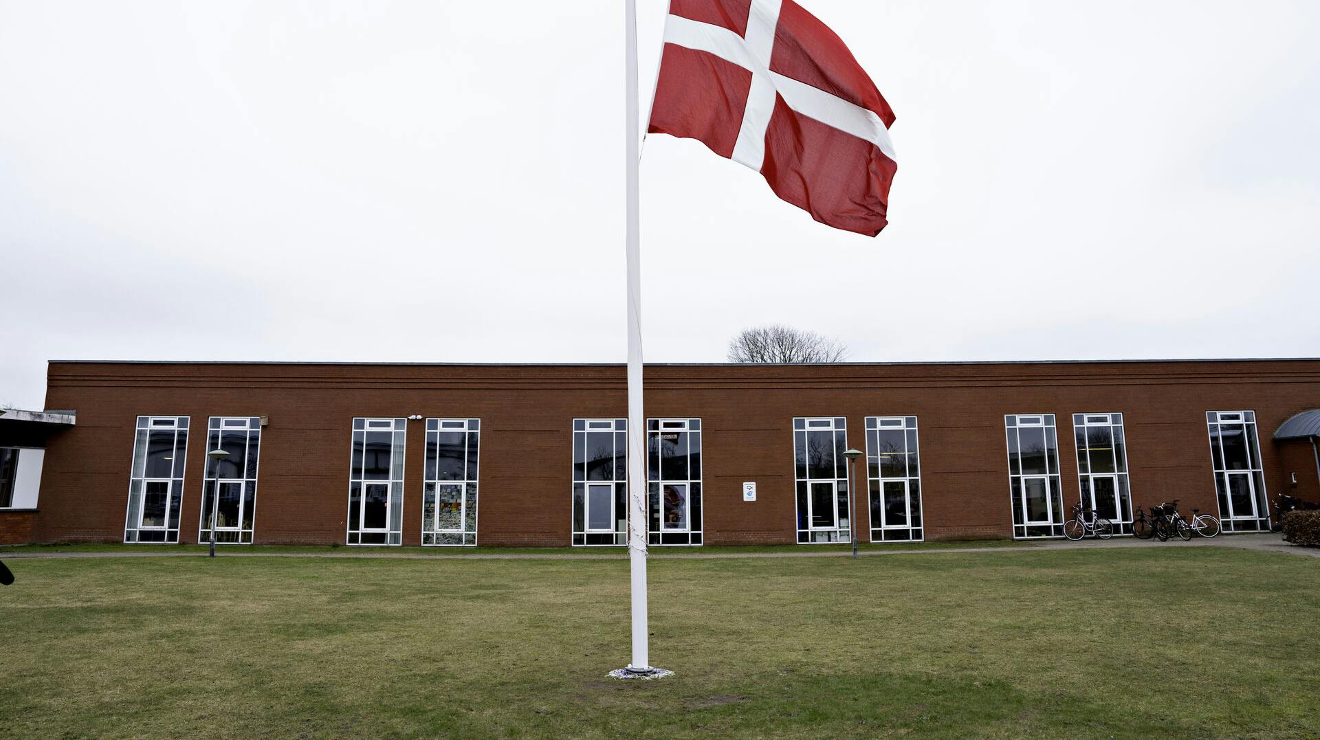 Der flages på halv stang ved Hjallerup Skole i Nordjylland tirsdag den 12. marts 2024. En 17-årig dreng er anholdt i sag om drab på 13-årig pige i Hjallerup, oplyser politiet. Ved foden af flagstamgen ligger blomster. (Foto: Henning Bagger/Ritzau Scanpix)